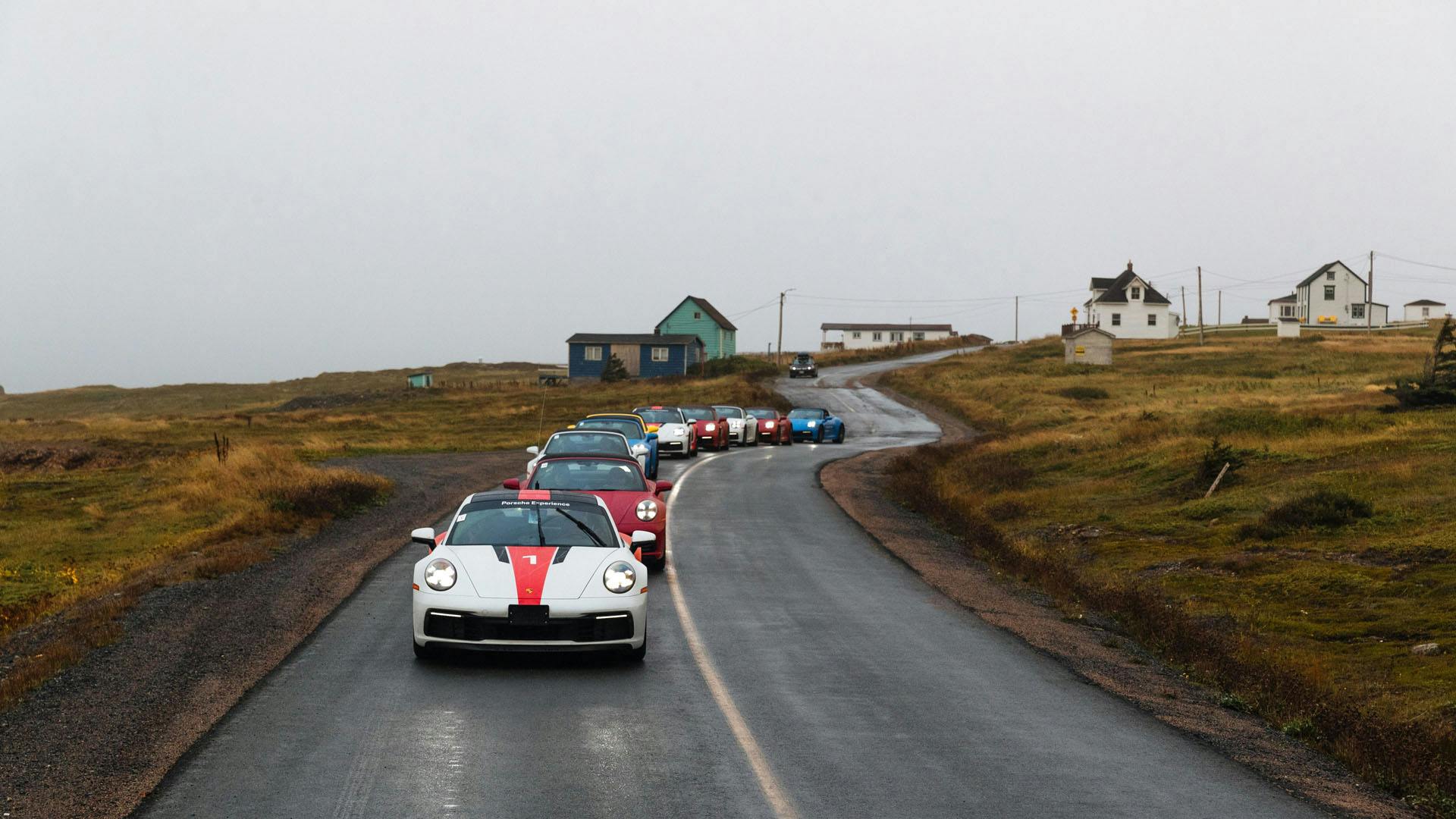 Un groupe de Porsche roulant en file indienne sur une route de campagne.