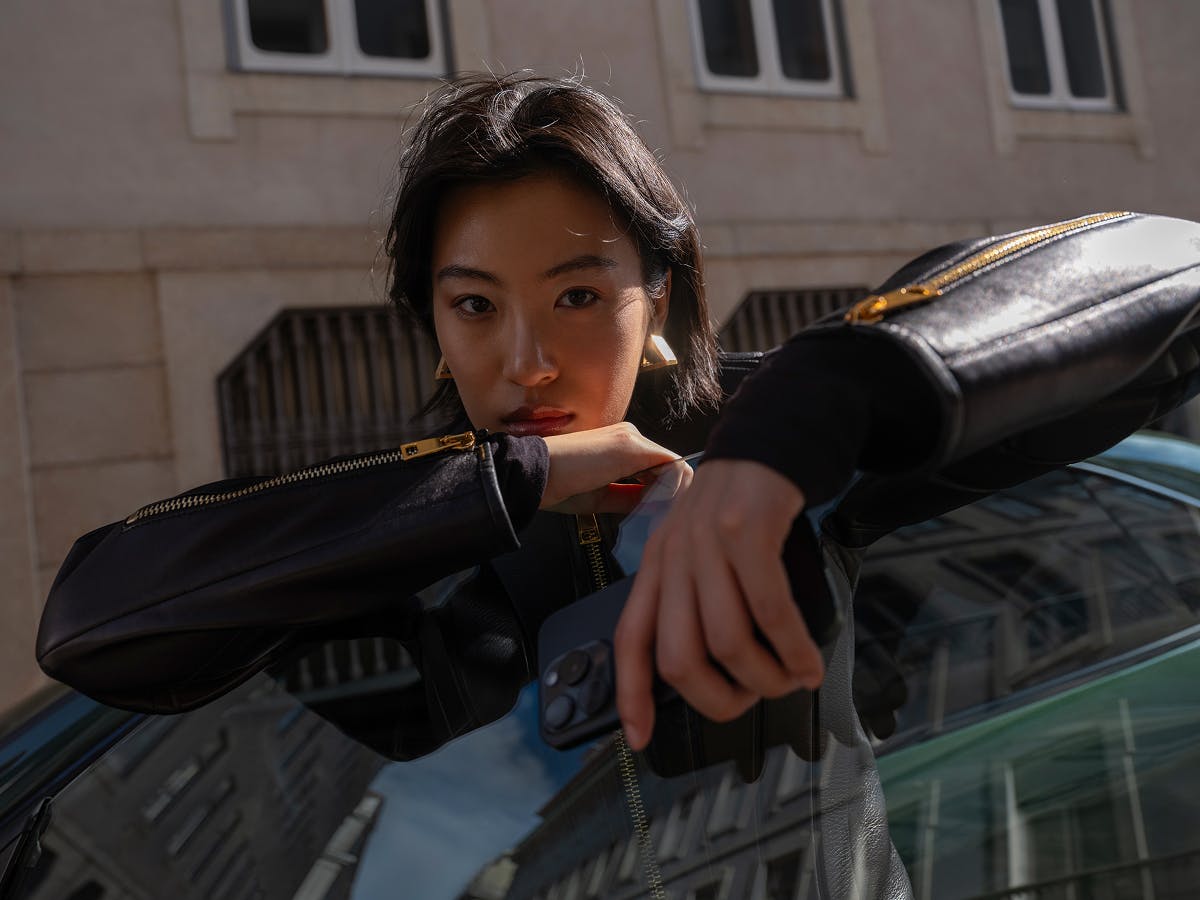 A woman standing in front of a Porsche and looking into the camera.