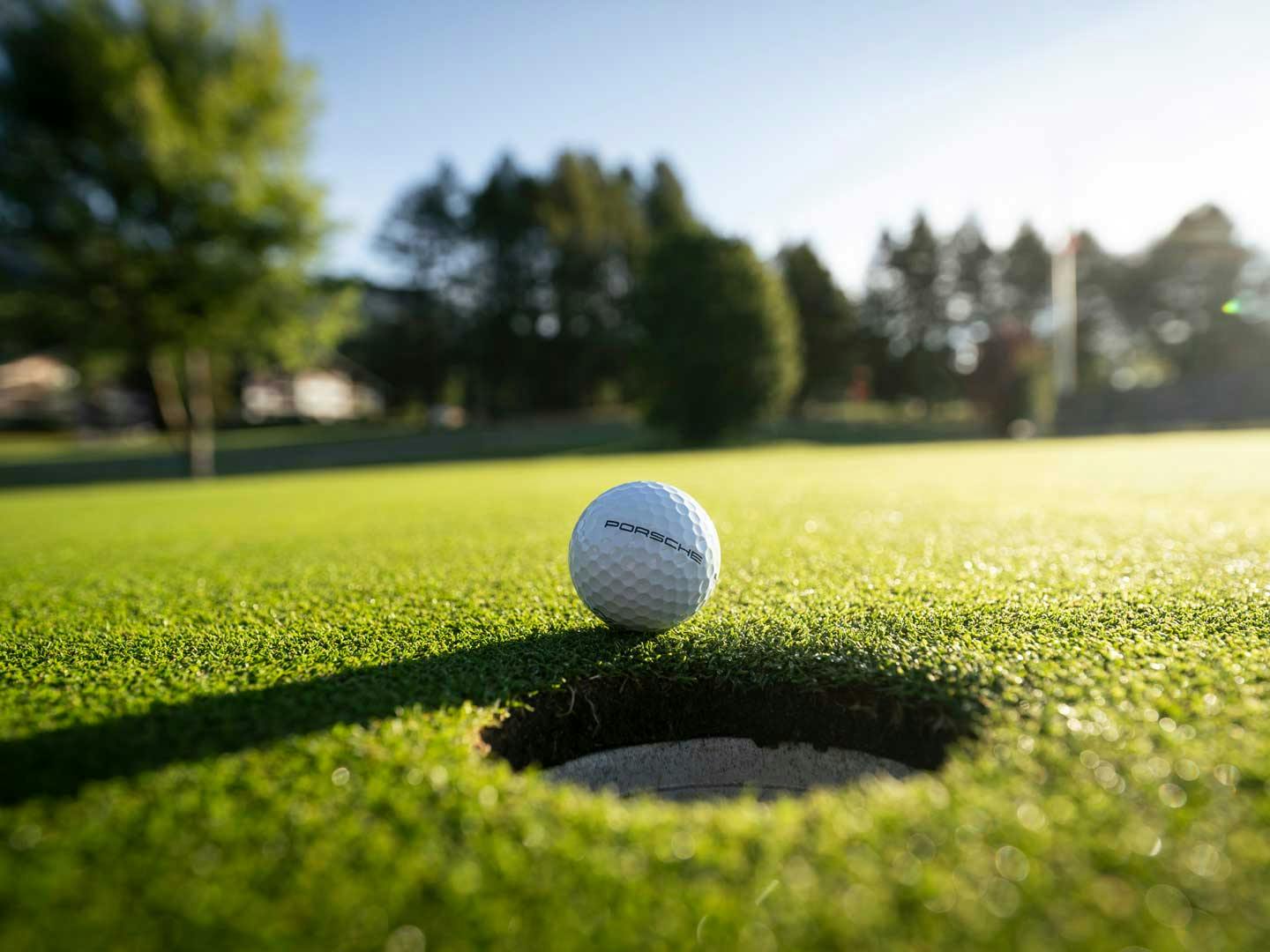 En vit golfboll med loggan för Porsche ligger på en golfbana med kortklippt grönt gräs.