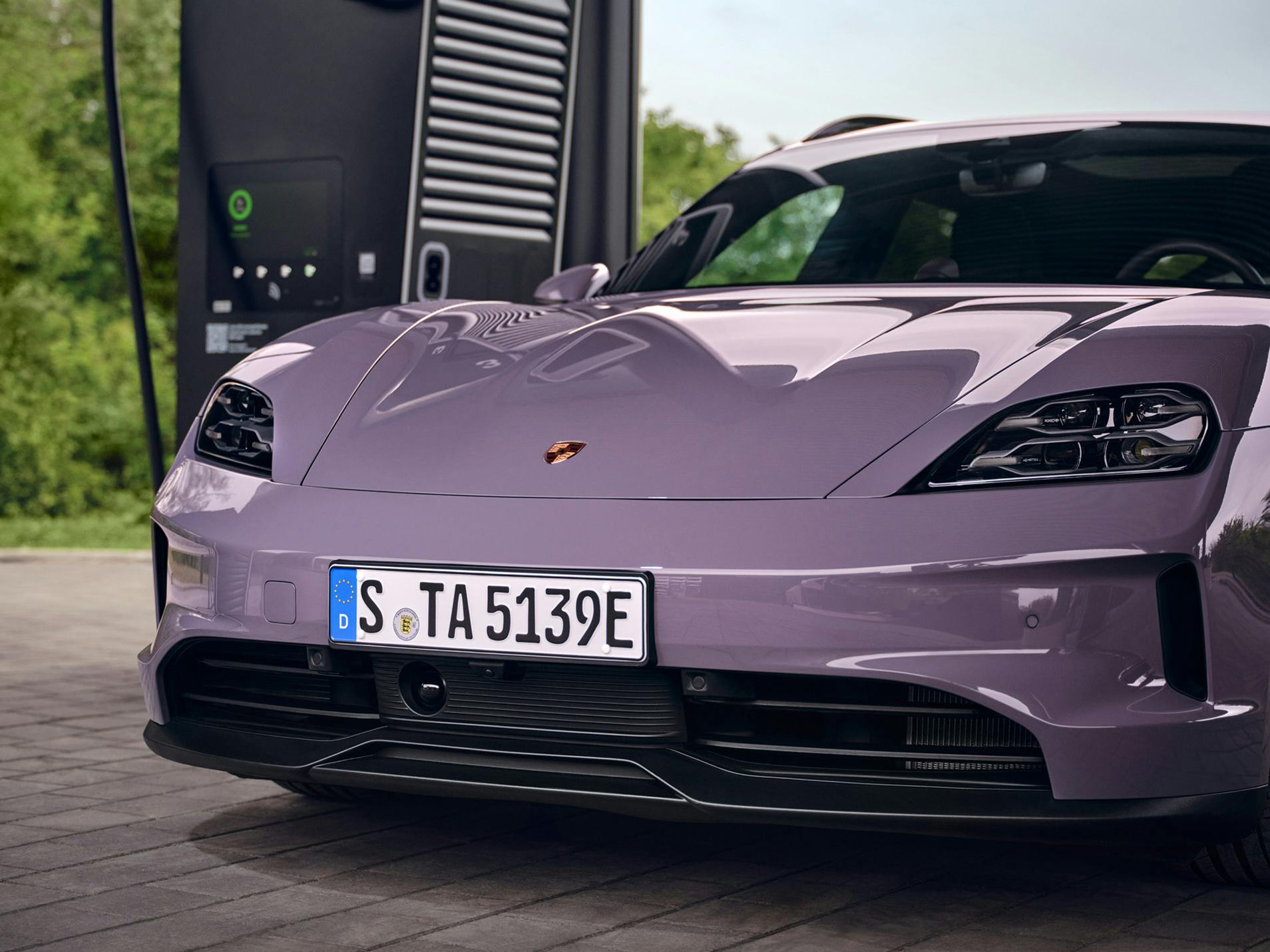 A Porsche Taycan Sport Turismo next to a charging pedestal. View of the front of the vehicle.