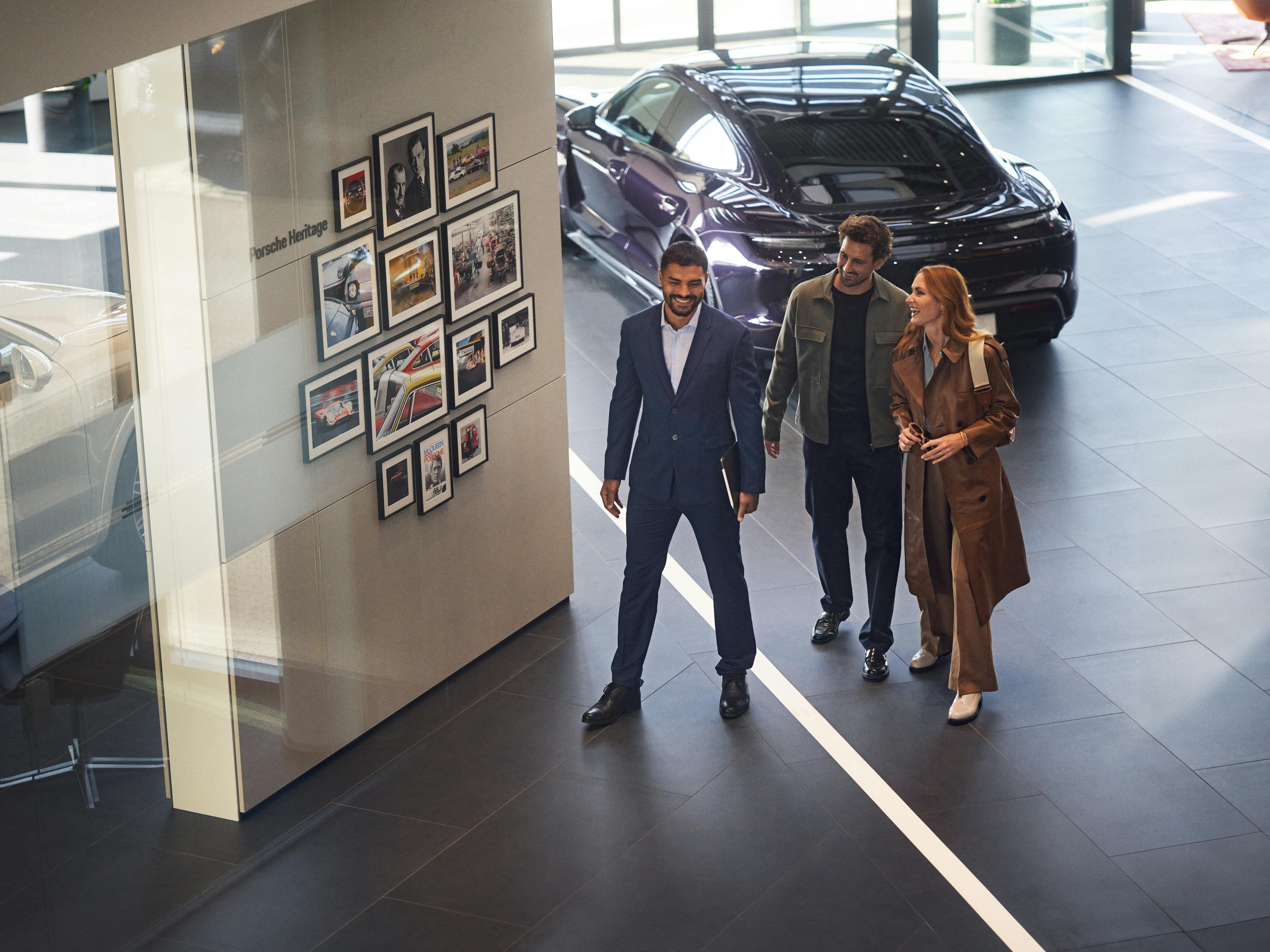 A Porsche member of staff walking and talking with customers in a Porsche Centre.