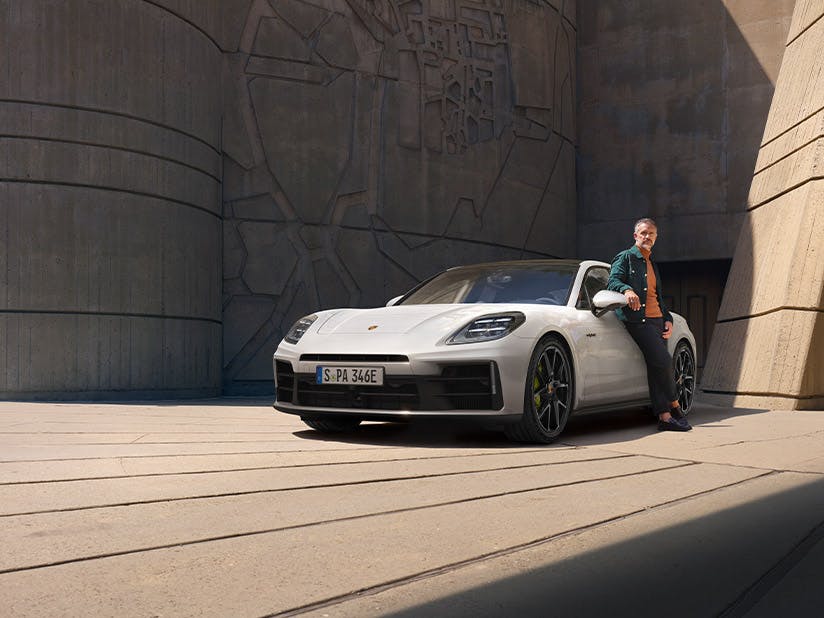 Weißer Porsche Panamera steht auf einem gepflasterten Platz, eine Person lehnt an der Fahrerseite.