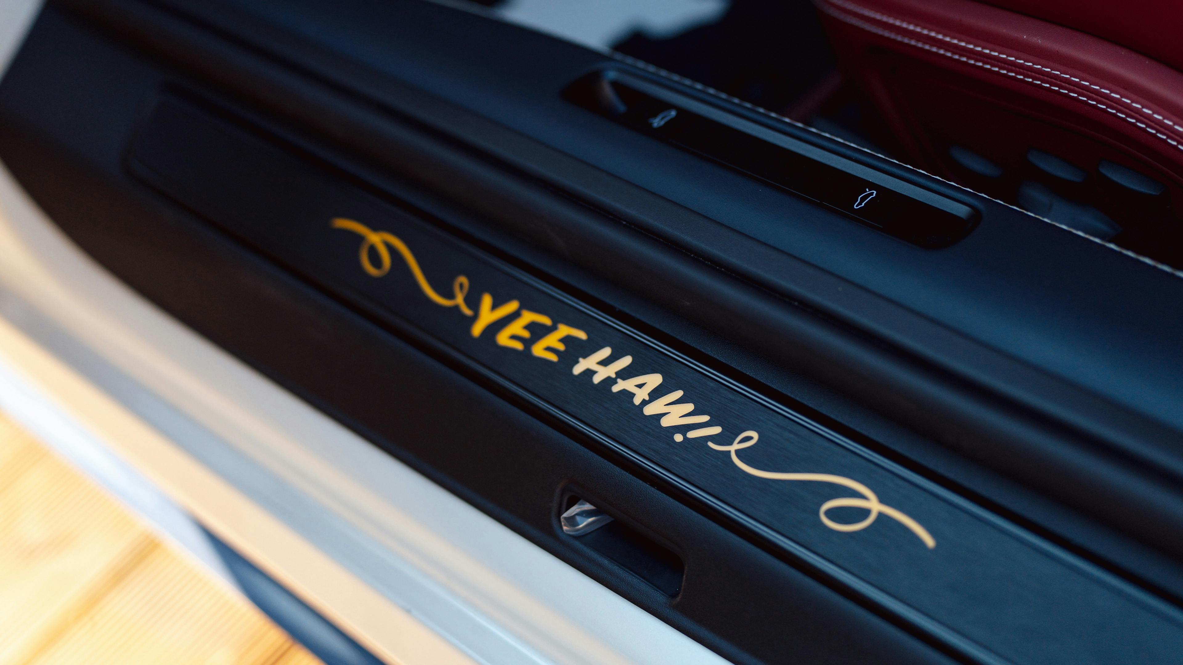 Close-up of a Porsche door sill featuring "Yee Haw!" script embroidery in gold, with a red leather interior.