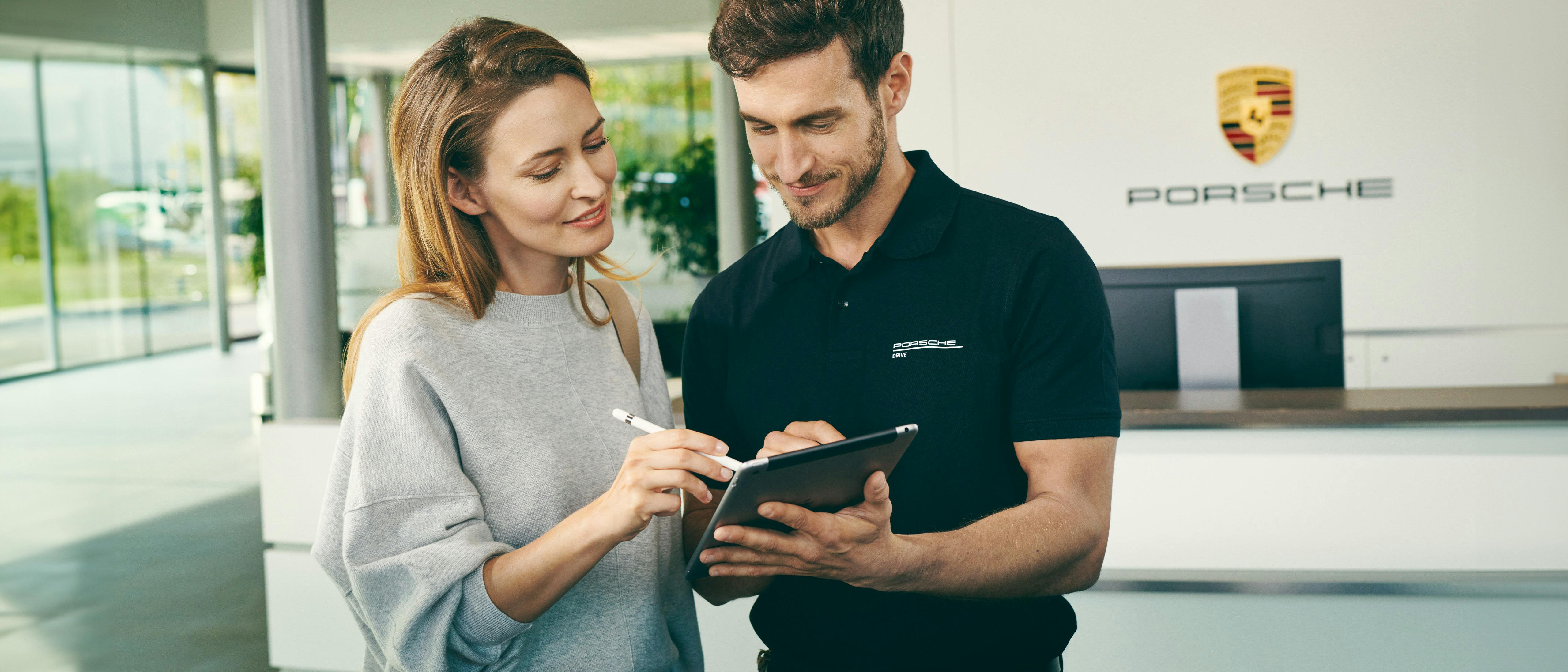 A customer signs on a tablet in a Porsche Center. An advisor holds the tablet.
