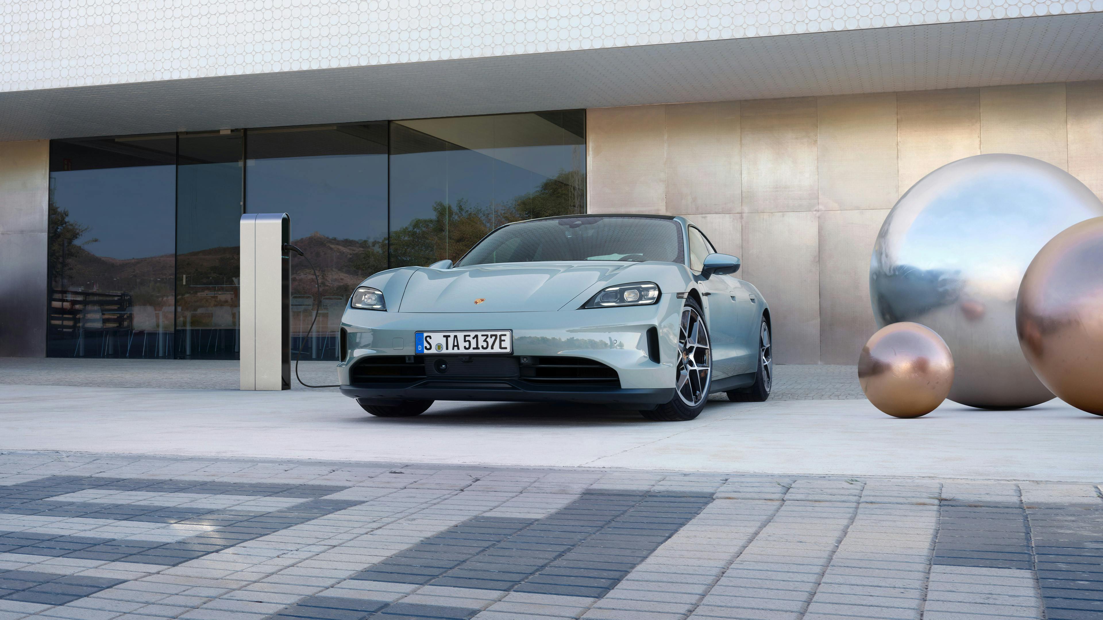A Porsche Taycan is parked at a charging station in front of a futuristic building.