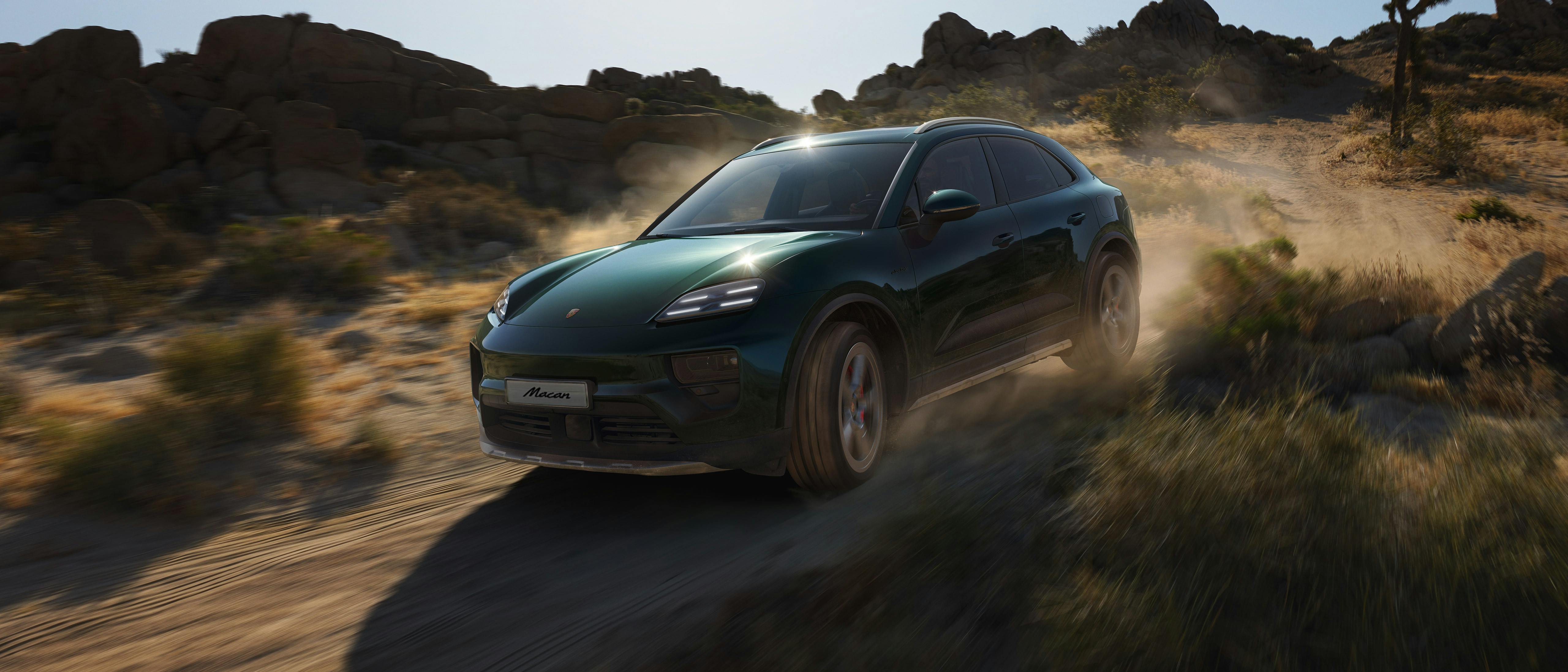 A green Porsche Macan drives dynamically through a dusty off-road terrain under sunlight, showcasing its sporty and rugged capabilities.