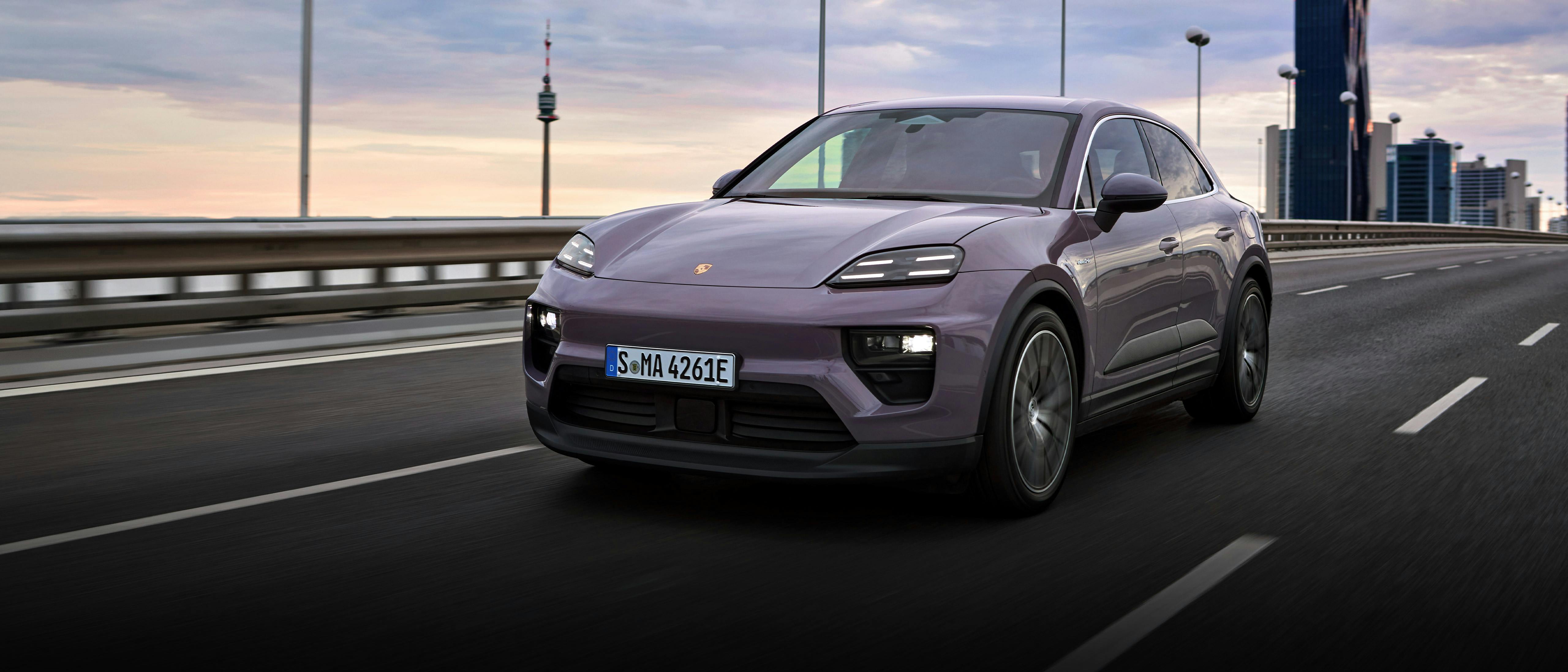 The Macan 4 Electric driving along a dual carriageway with tall office buildings visible in the background.
