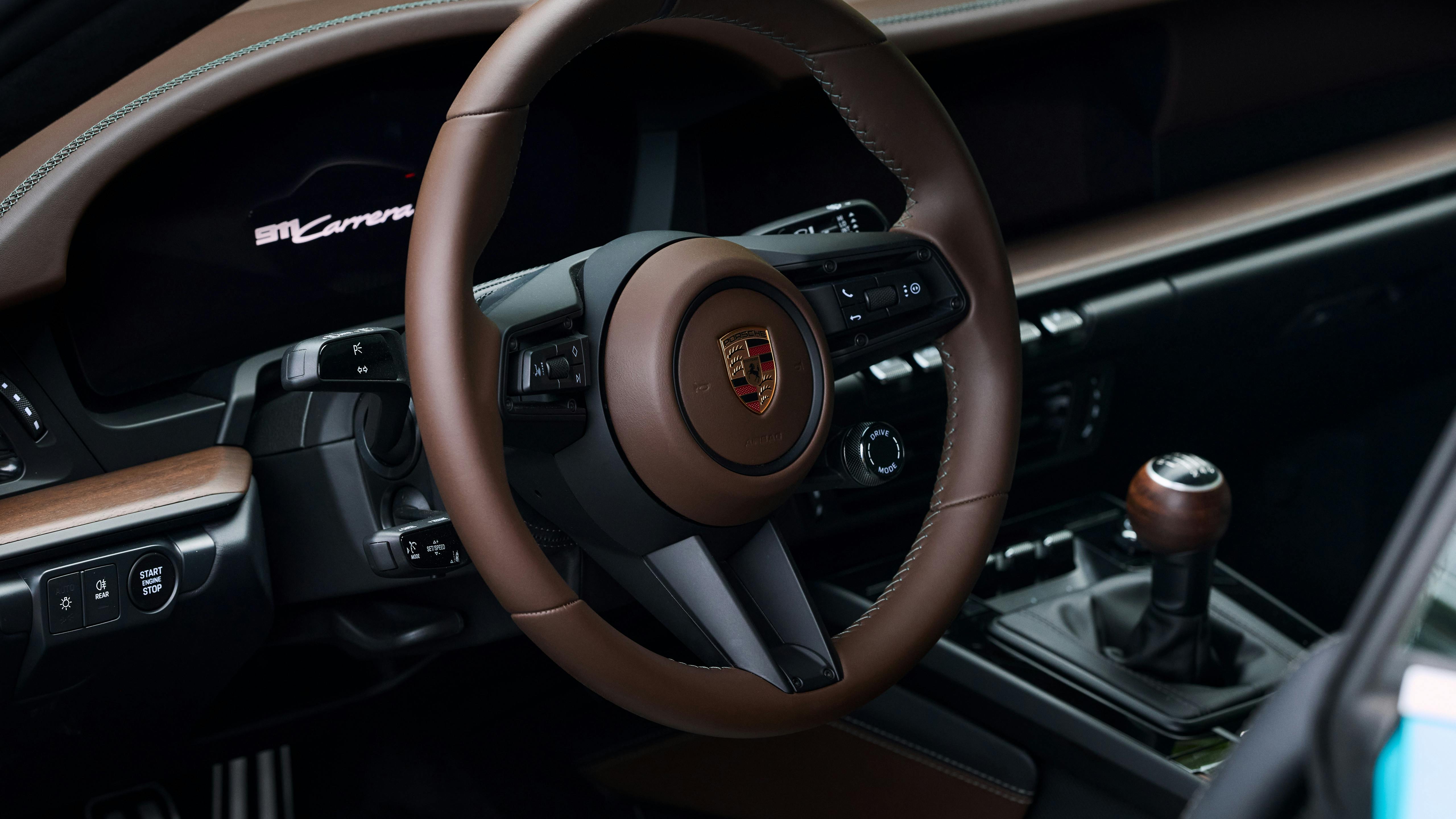Close-up of Porsche 911 Carrera cockpit with brown leather steering wheel and manual gear lever.