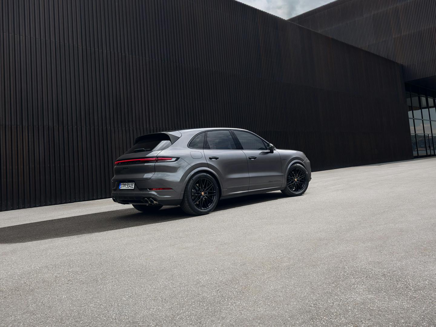 The Cayenne E-Hybrid Black Edition parked outside a modern building that is made up of dark textured material and also glass.