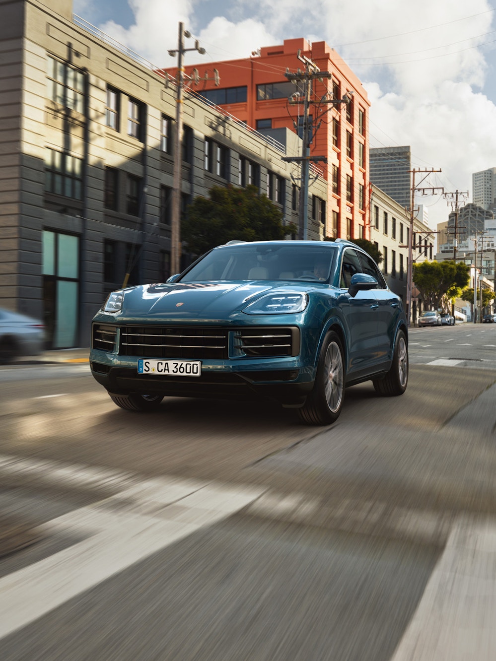 A blue metallic Porsche Cayenne driving on a urban street.
