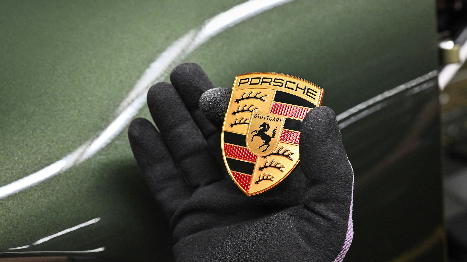 Gloved hand holding the Porsche crest badge against the British Racing Green bodywork of the Earls Court 51 Edition 911.​