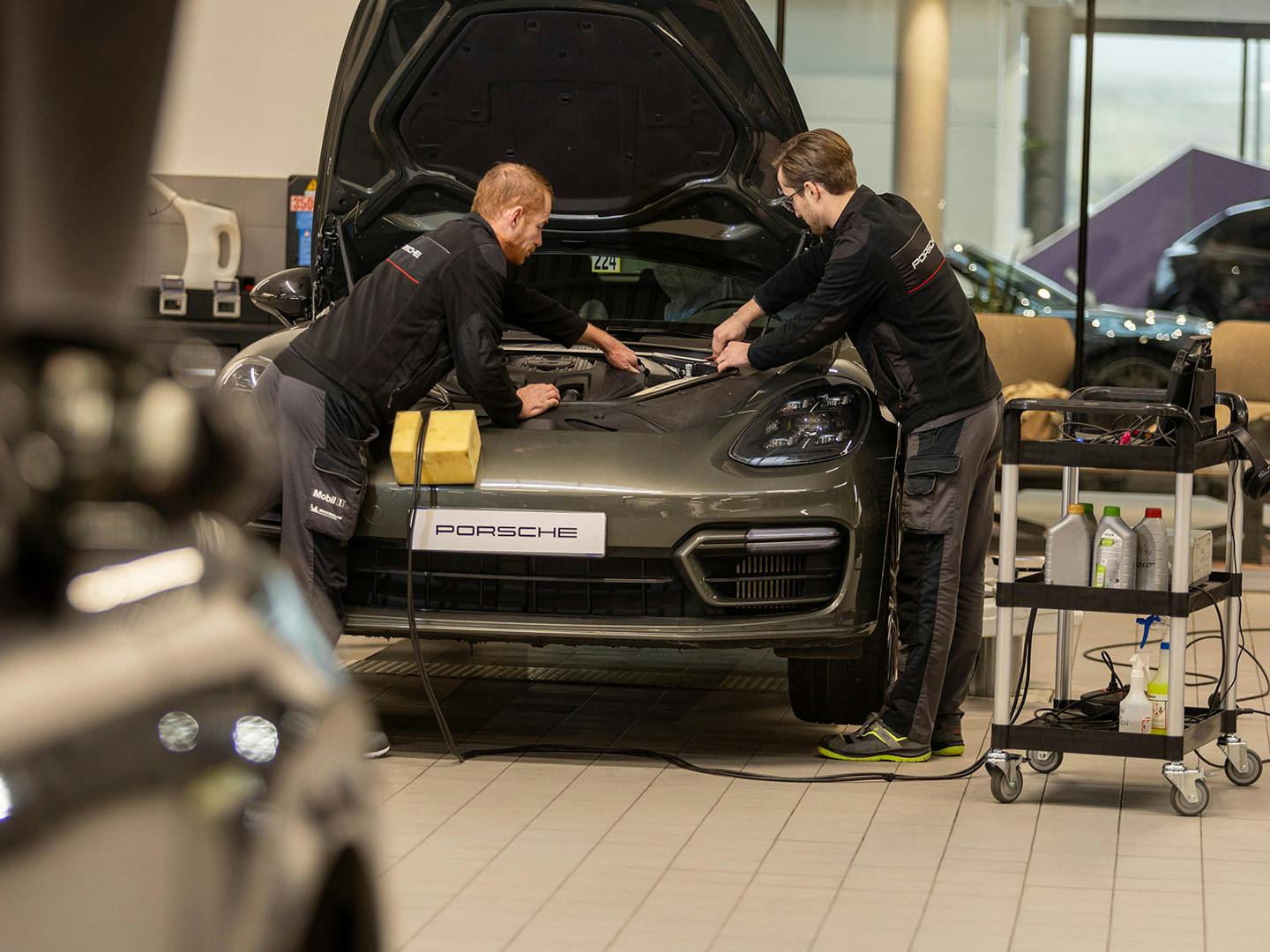 Deux techniciens Porsche travaillent sous le capot d'un véhicule Porsche.