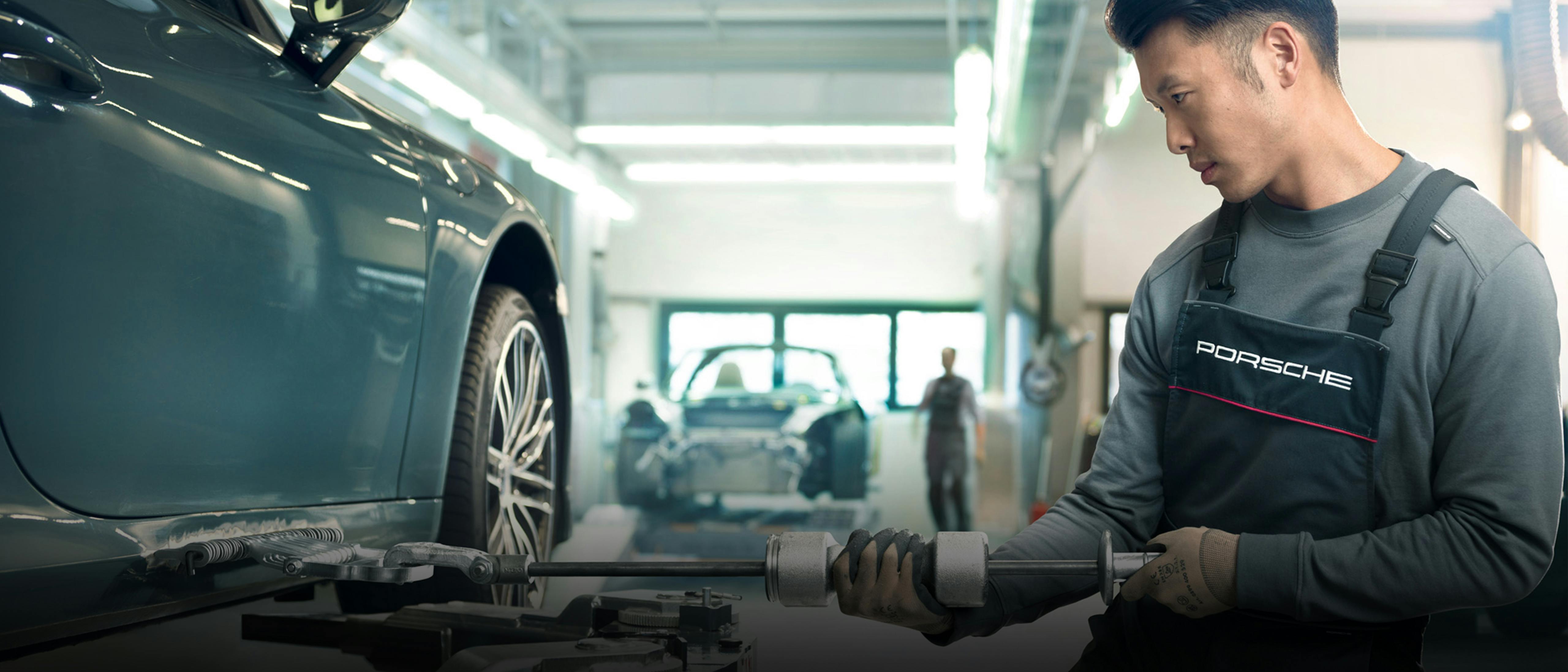 A Porsche technician repairs a car's body using specialized tools in a workshop, showcasing precision and expertise in automotive restoration