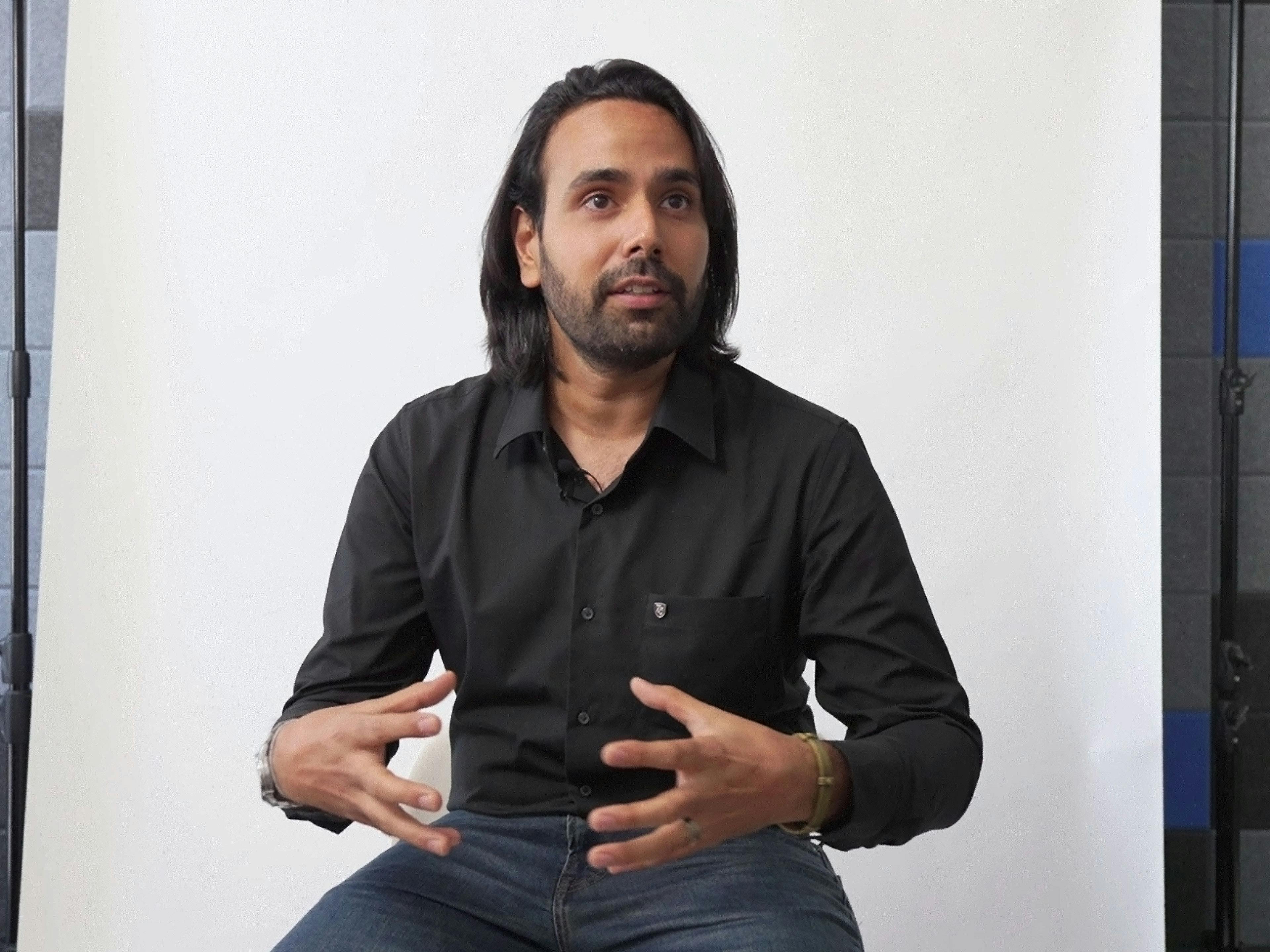 Porsche employee Konain sitting in front of the camera in an interview and talking while gesturing.