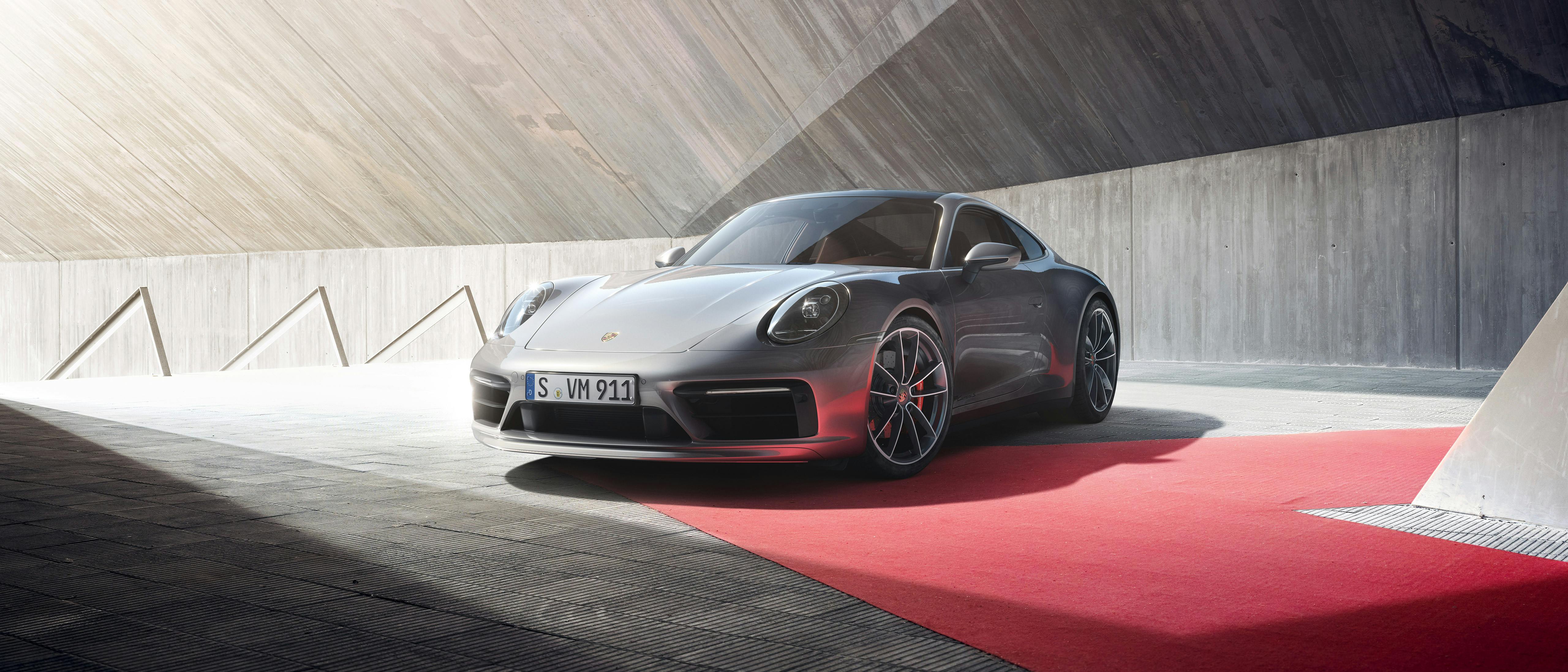 Ein Porsche 911 steht auf einem roten Teppich vor moderner Betonarchitektur.