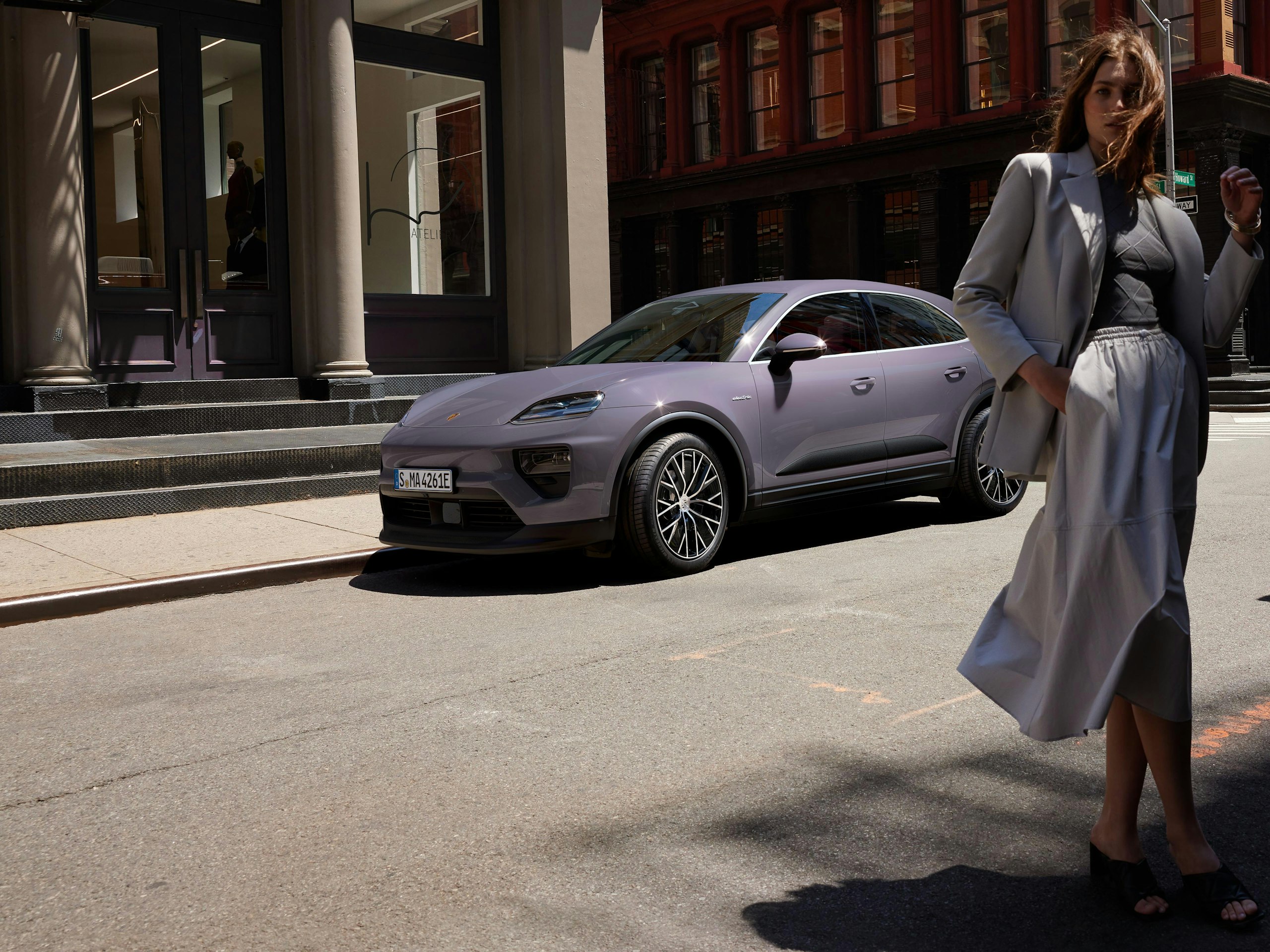 A woman walks in front of a Macan on a city street.
