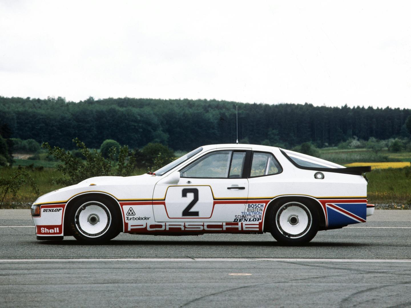 A side view of the white Porsche 924 Carrera GTP race car with red and blue stripes and the number 2, on track.