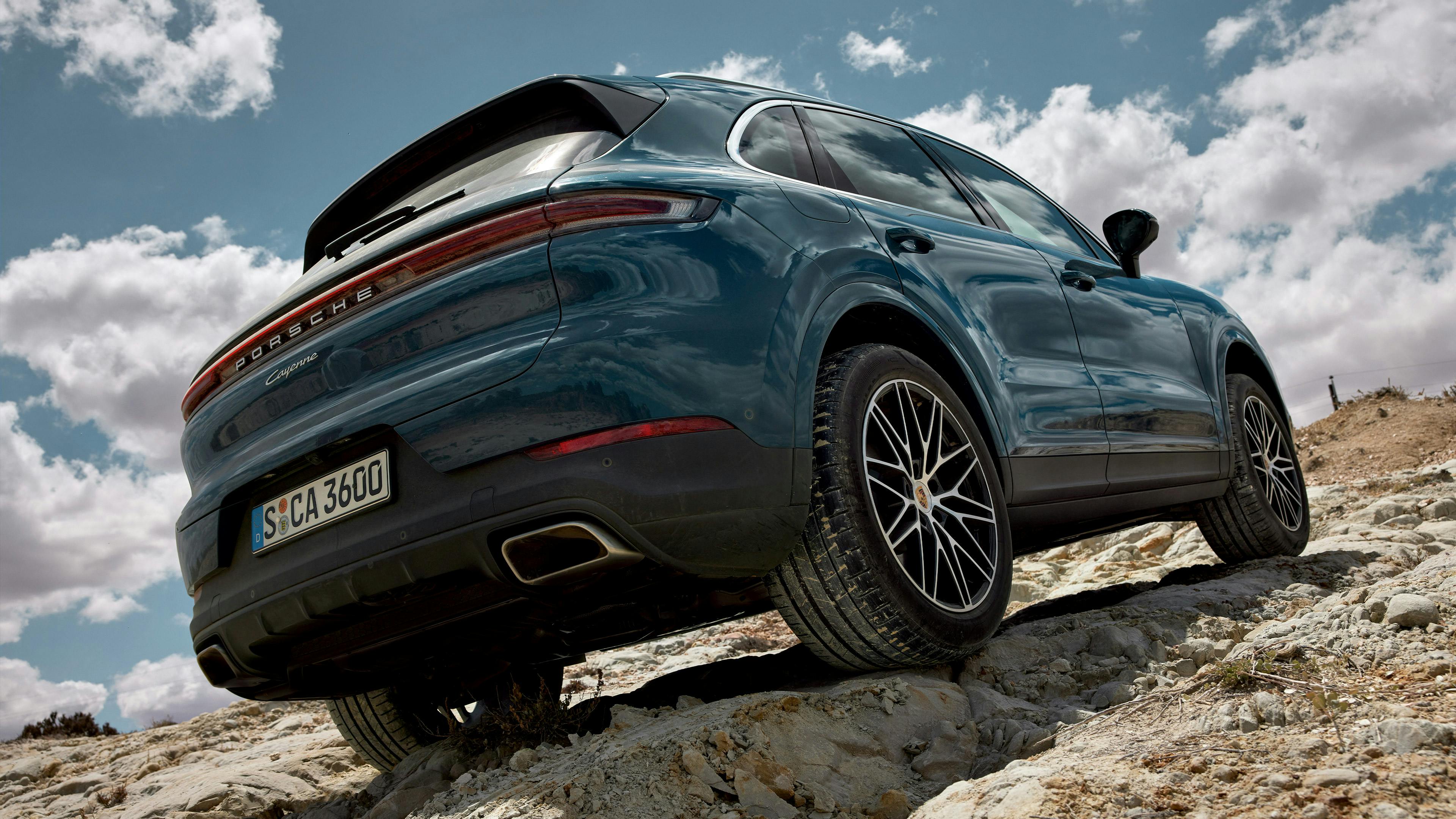 Une Porsche Cayenne bleue se dresse sur des rochers dans une vue dynamique de l'arrière et du côté.