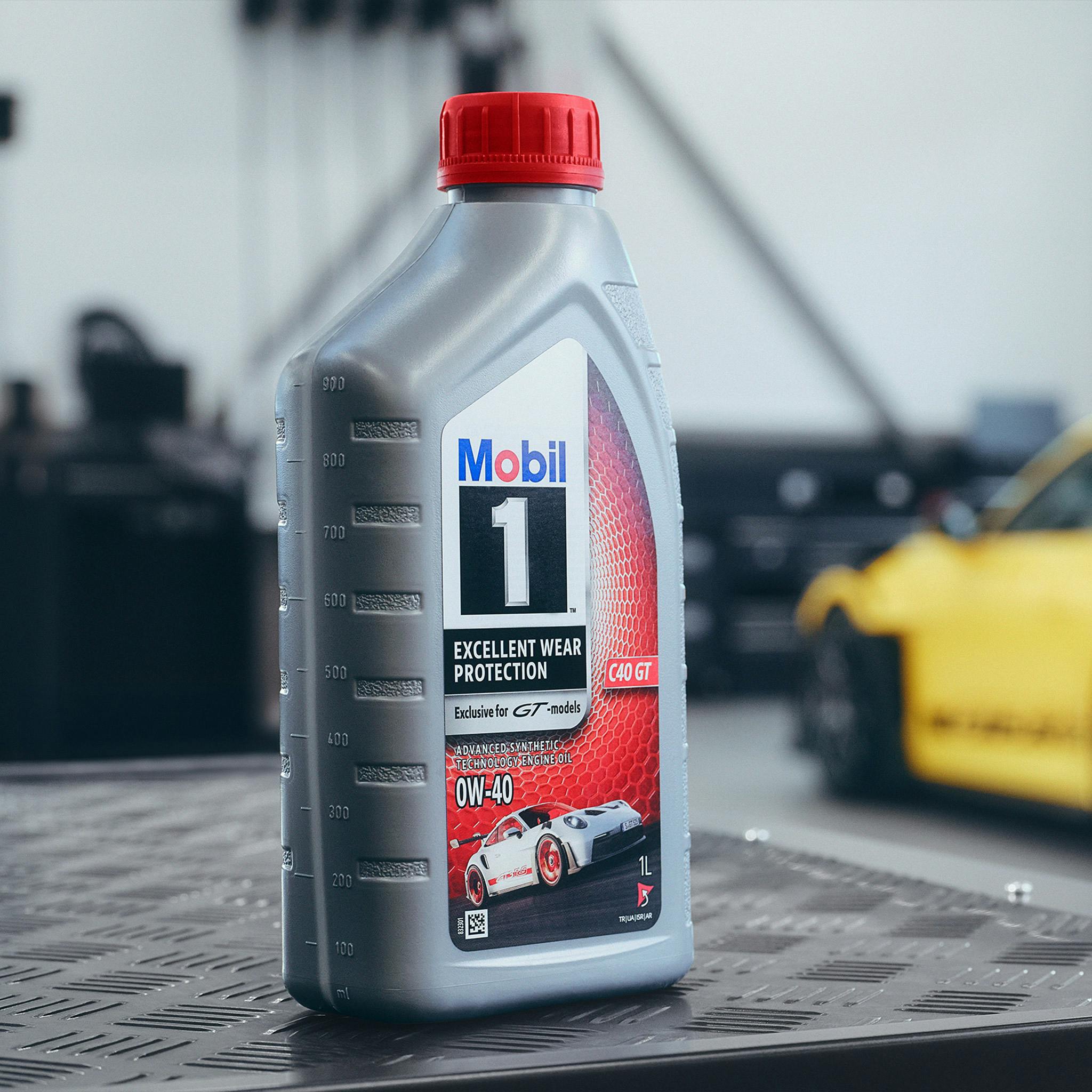 In the foreground is a Mobil 1 oil bottle. A Porsche 911 can be seen in the background.