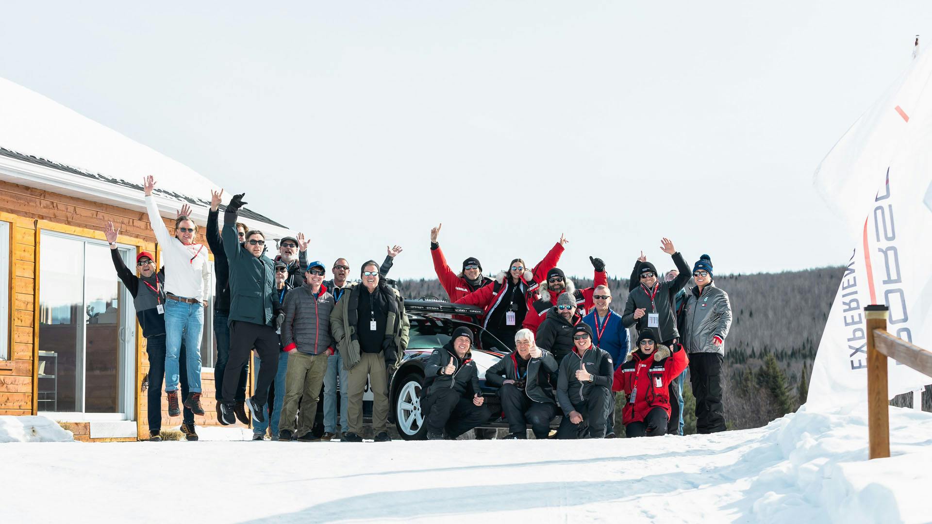 Un grand groupe de personnes dans un décor hivernal enneigé posant devant la Porsche.