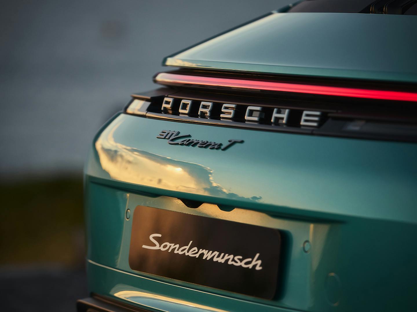 Detail of a turquoise Porsche 911 Carrera rear with illuminated light strip, Porsche lettering and model badge.