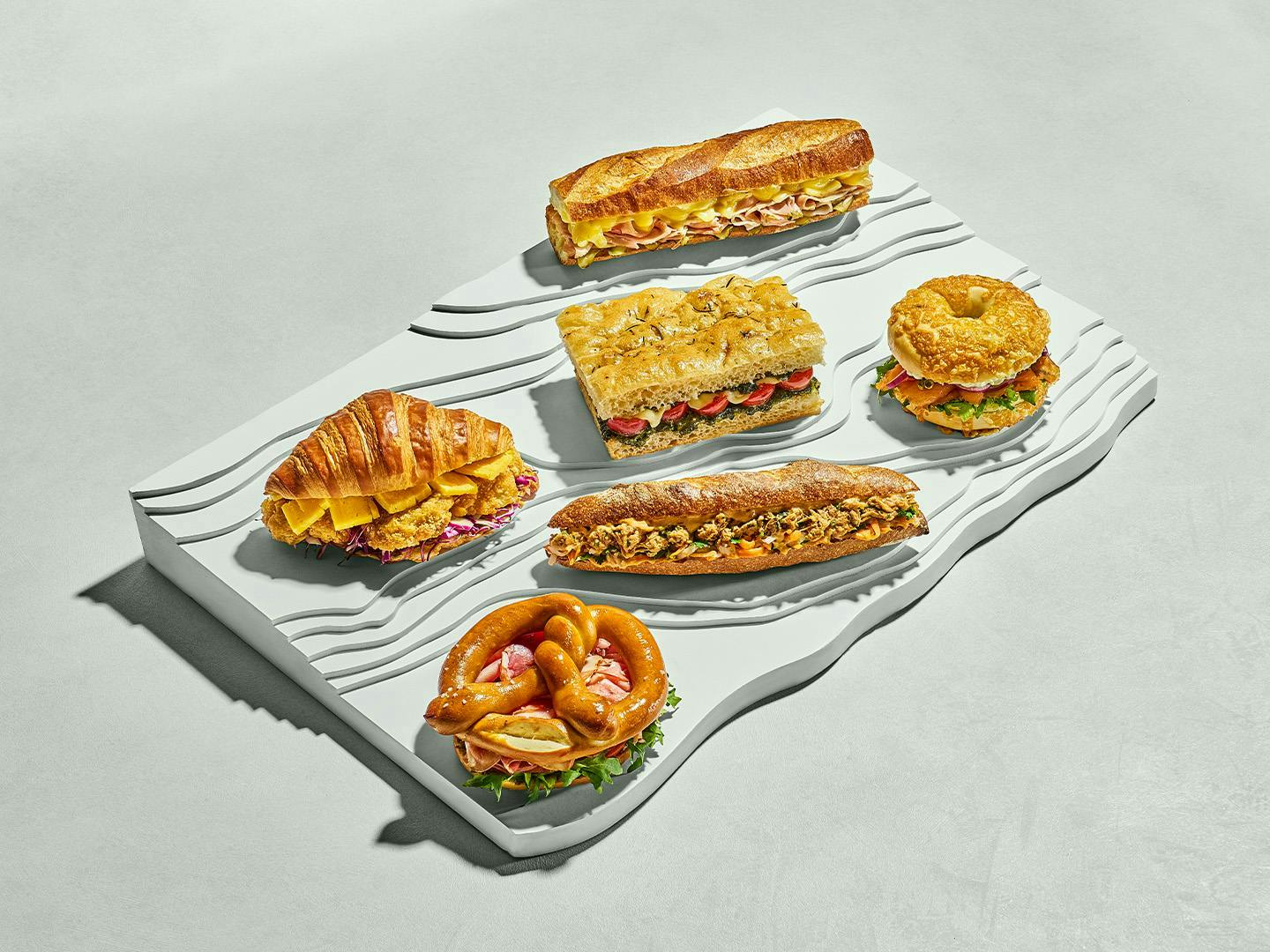 Selection of filled pastries and sandwiches including croissant, focaccia, pretzel and baguette on display.