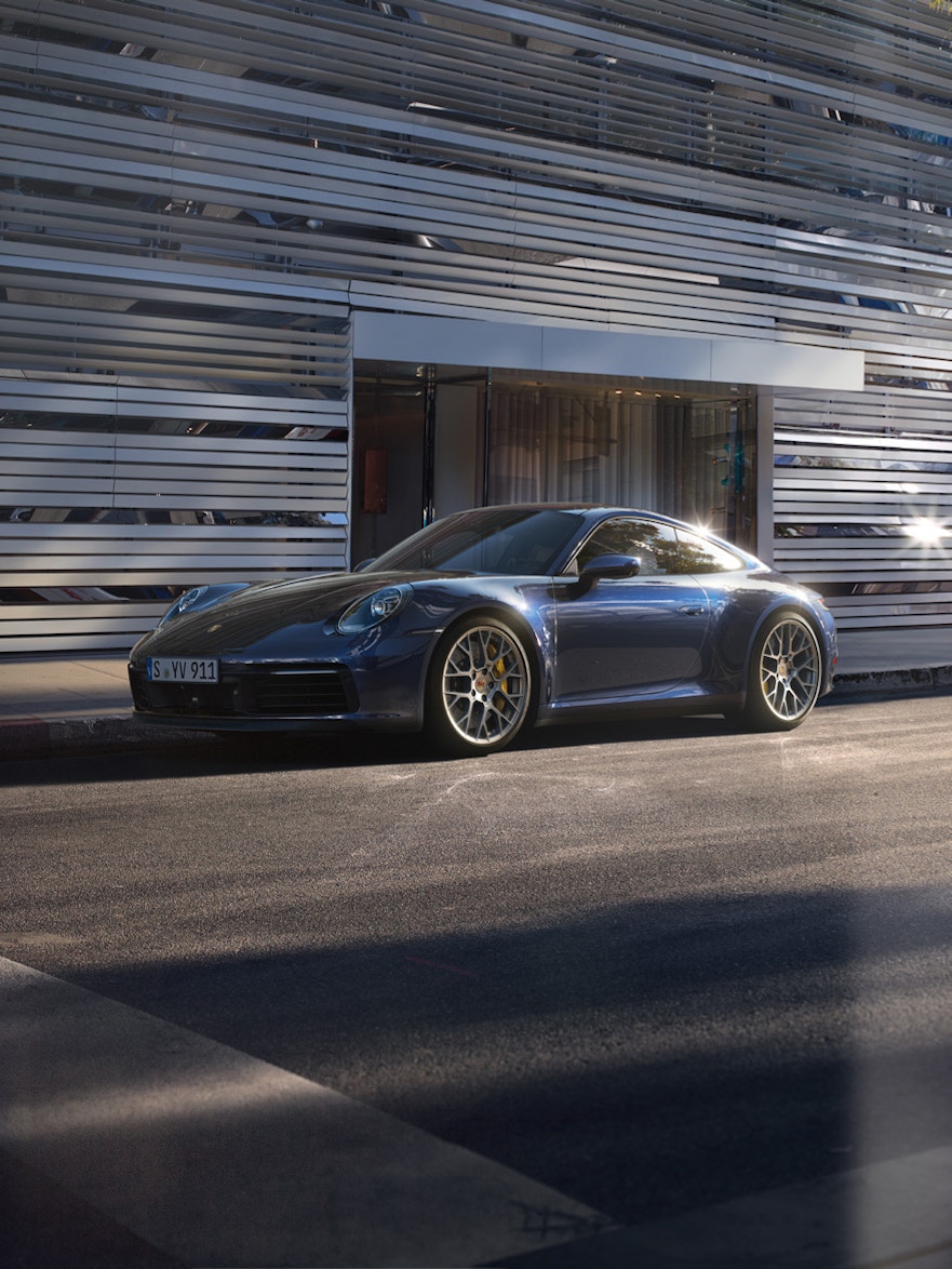 Ein Porsche 911 Carrera 4S, der draußen auf der Straße geparkt ist, mit einem großen Gebäude im Hintergrund.