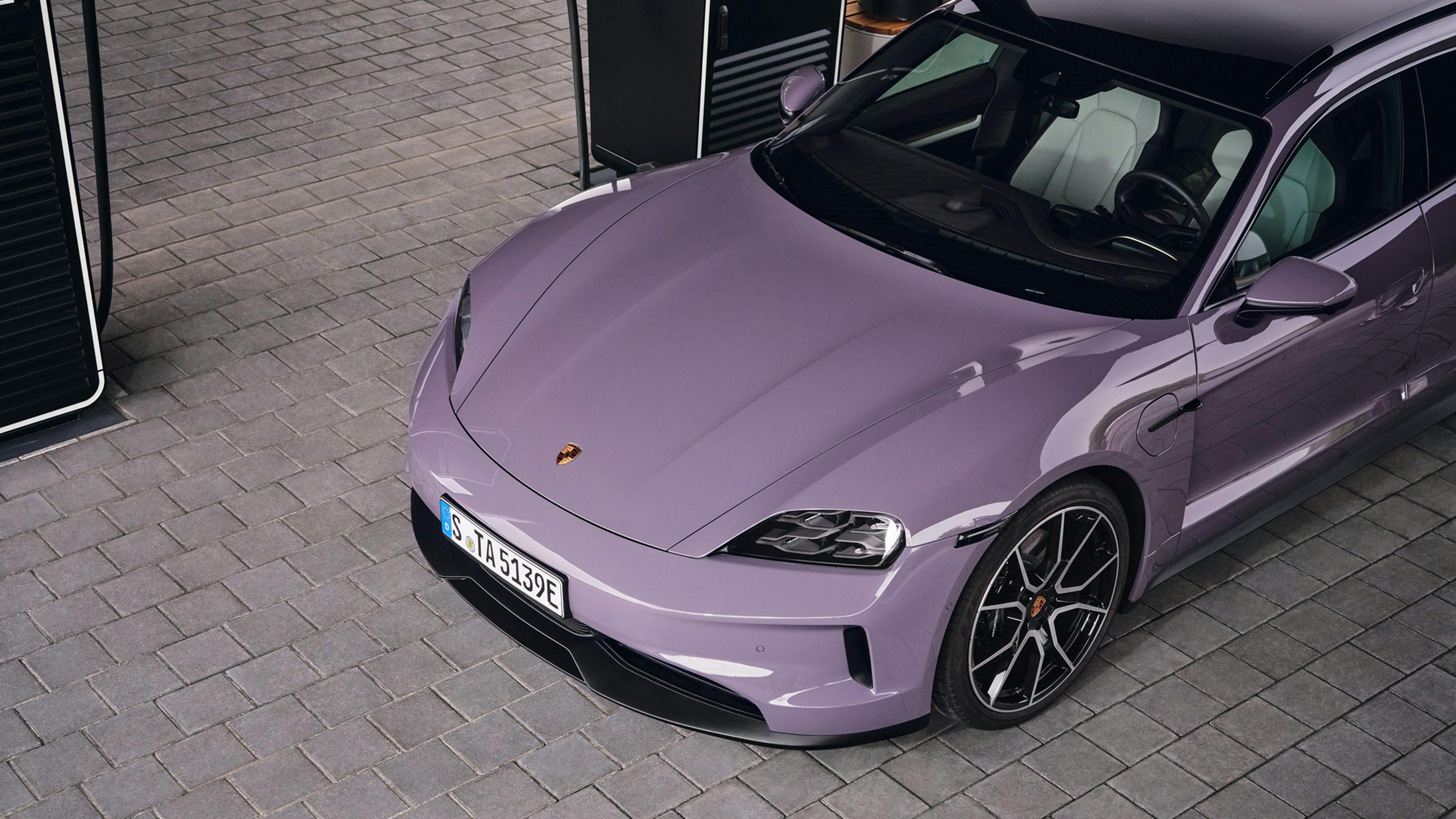 A Porsche Taycan Sport Turismo next to a charging pedestal at a Porsche Charging Lounge.