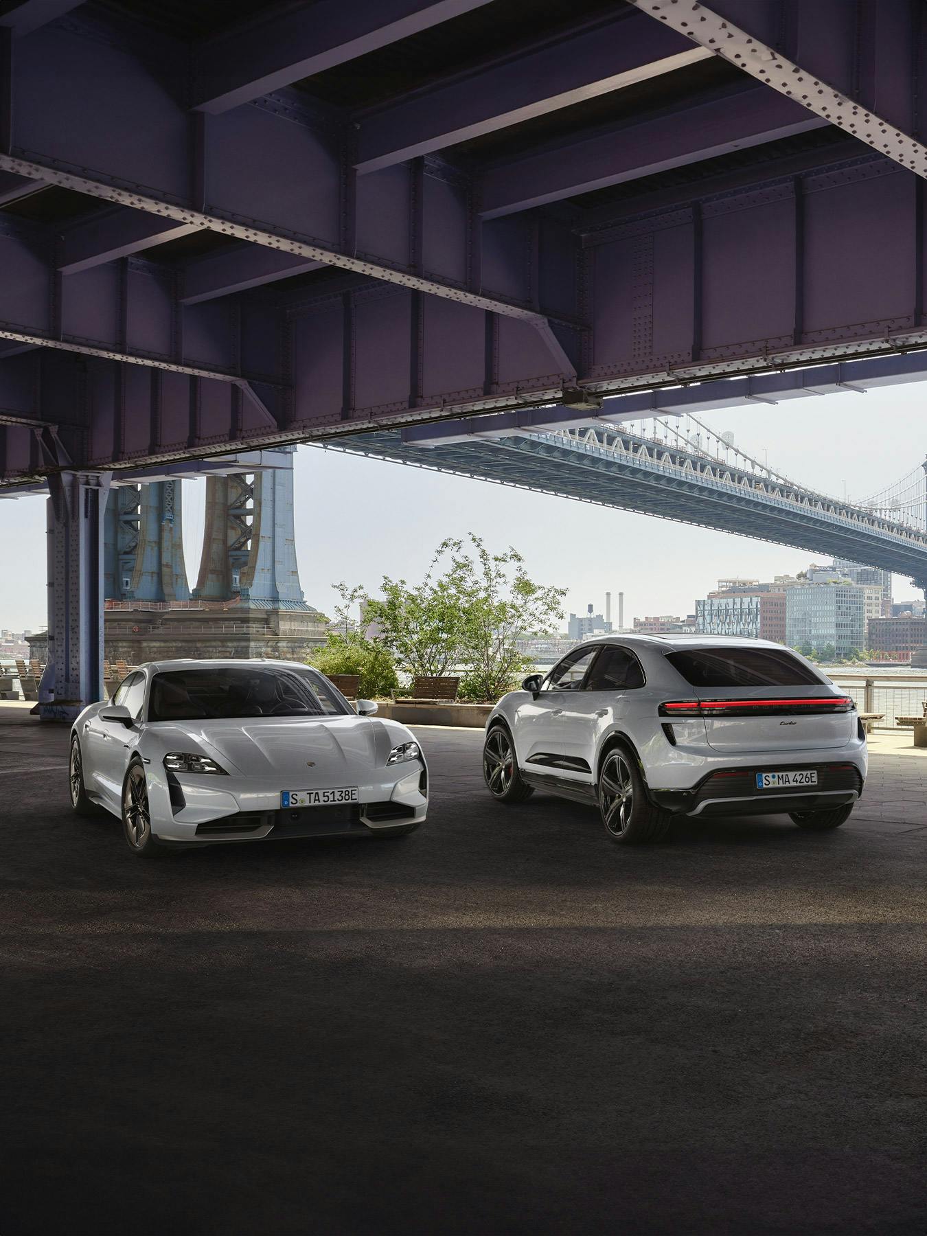 The new all-electric Taycan and Macan Turbo parked alongside each other, under a bridge.