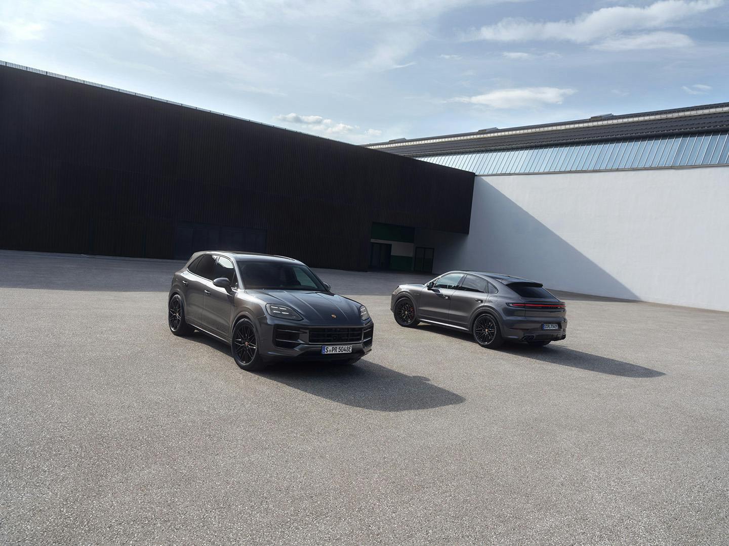 Δύο Porsche Cayenne Black Edition, μία coupe και μία SUV, την ημέρα, δίπλα δίπλα, αντιπαράλληλα και εν στάσει σε προαύλιο χώρο.
