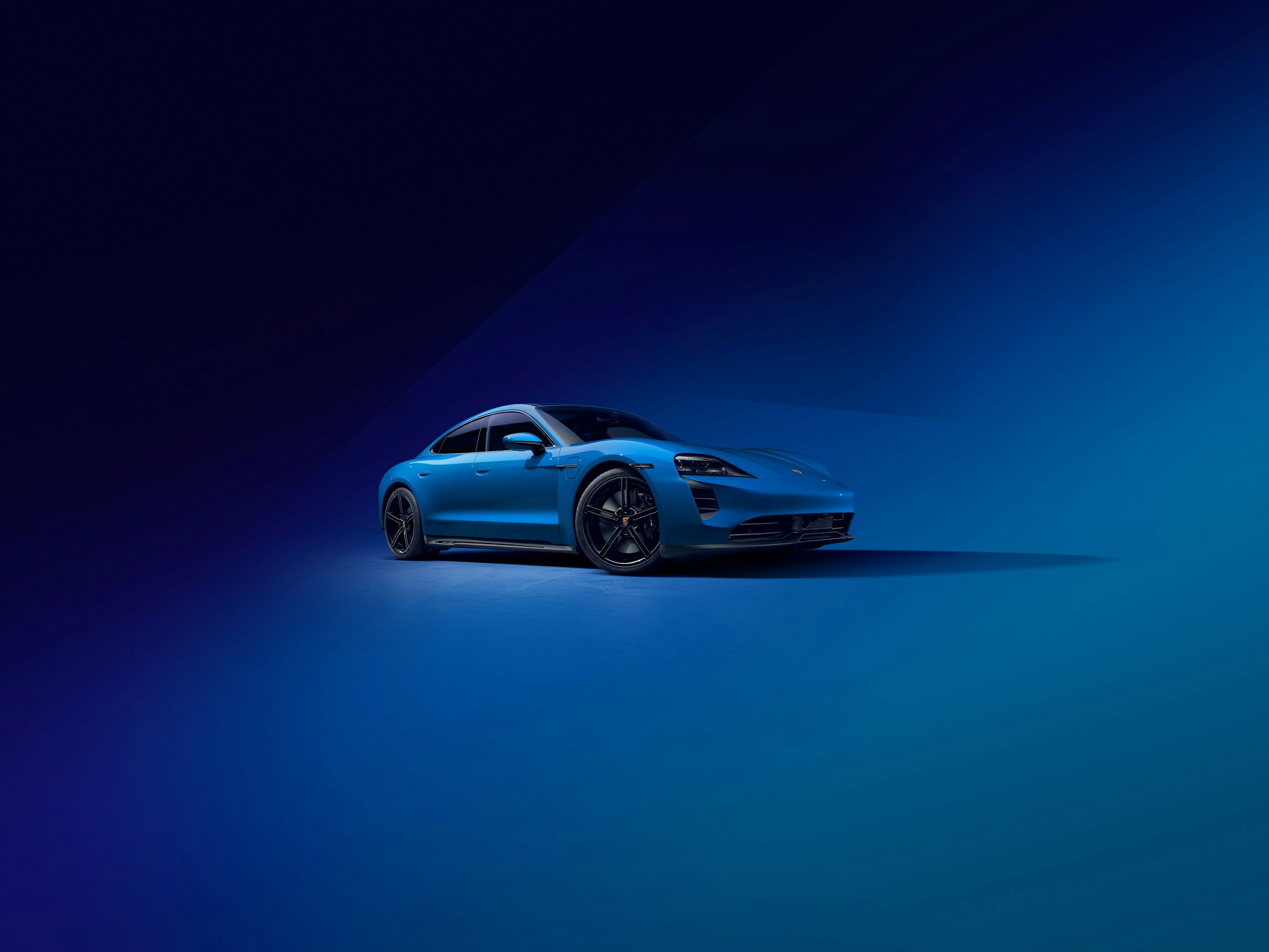 Side shot of a blue Taycan GTS standing in front of an abstract blue background