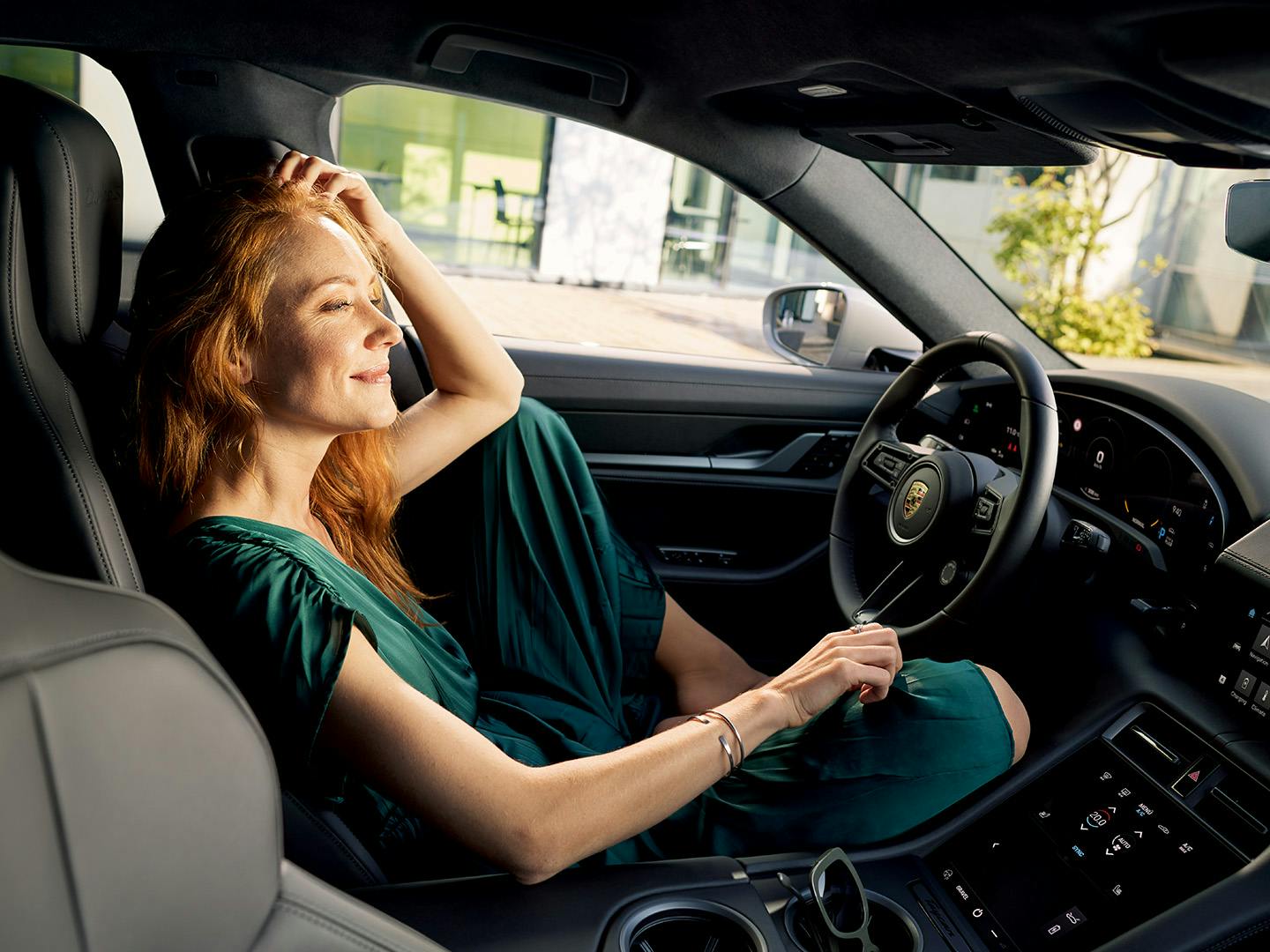 A woman relaxing in driver's seat of Porsche, hand on forehead, eyes closed in moment of contentment.