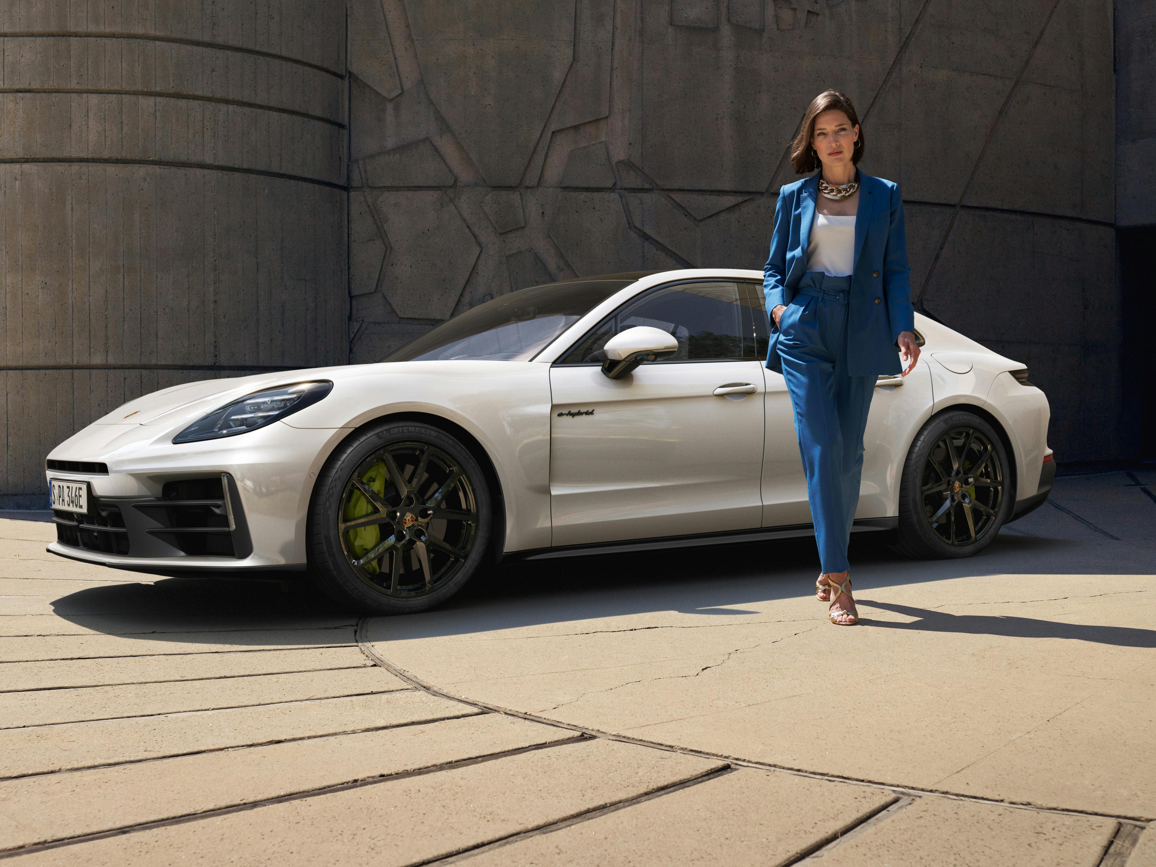 The Panamera 4 E-Hybrid parked near a stone building, with a woman walking away from the car.