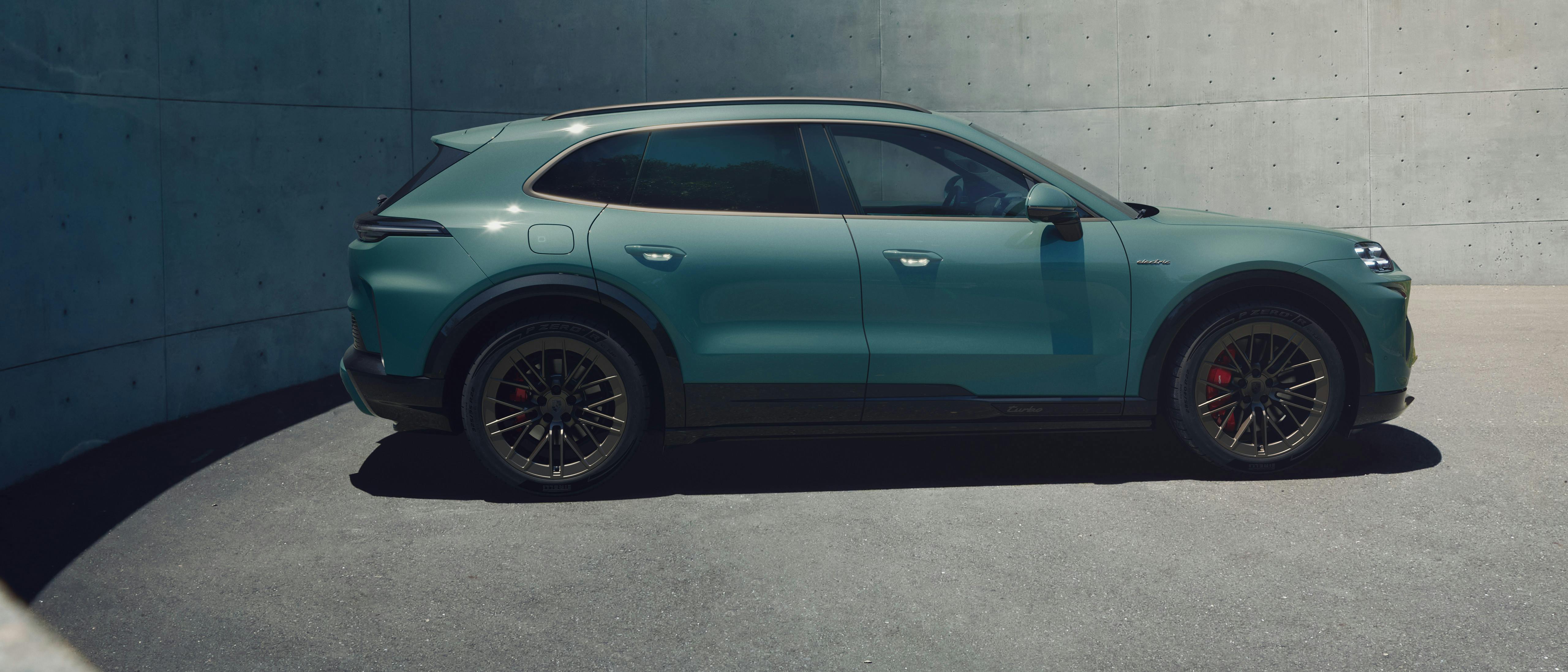 A Cayenne Electric parked in front of a grey brick wall. In the distance, there is a brown structure of a building and greens trees.
