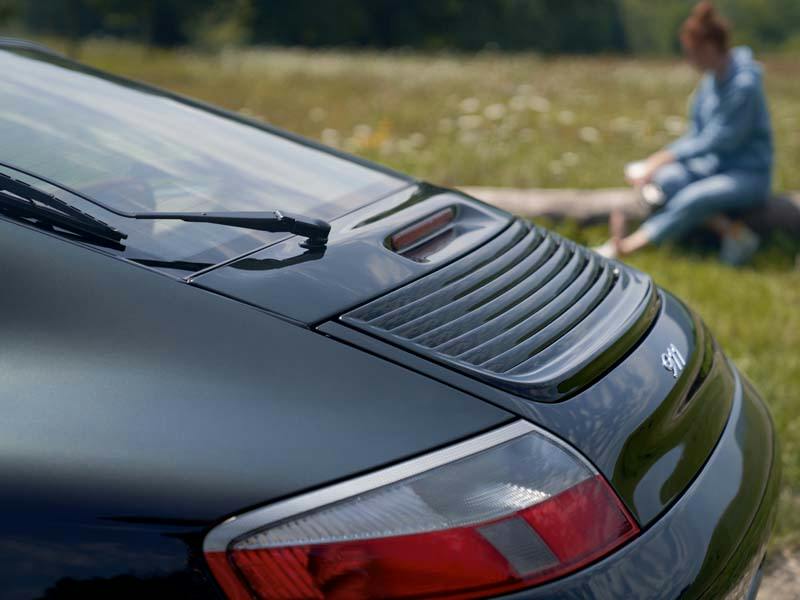 Heck eines schwarzen Porsche 911 auf einer Wiese.