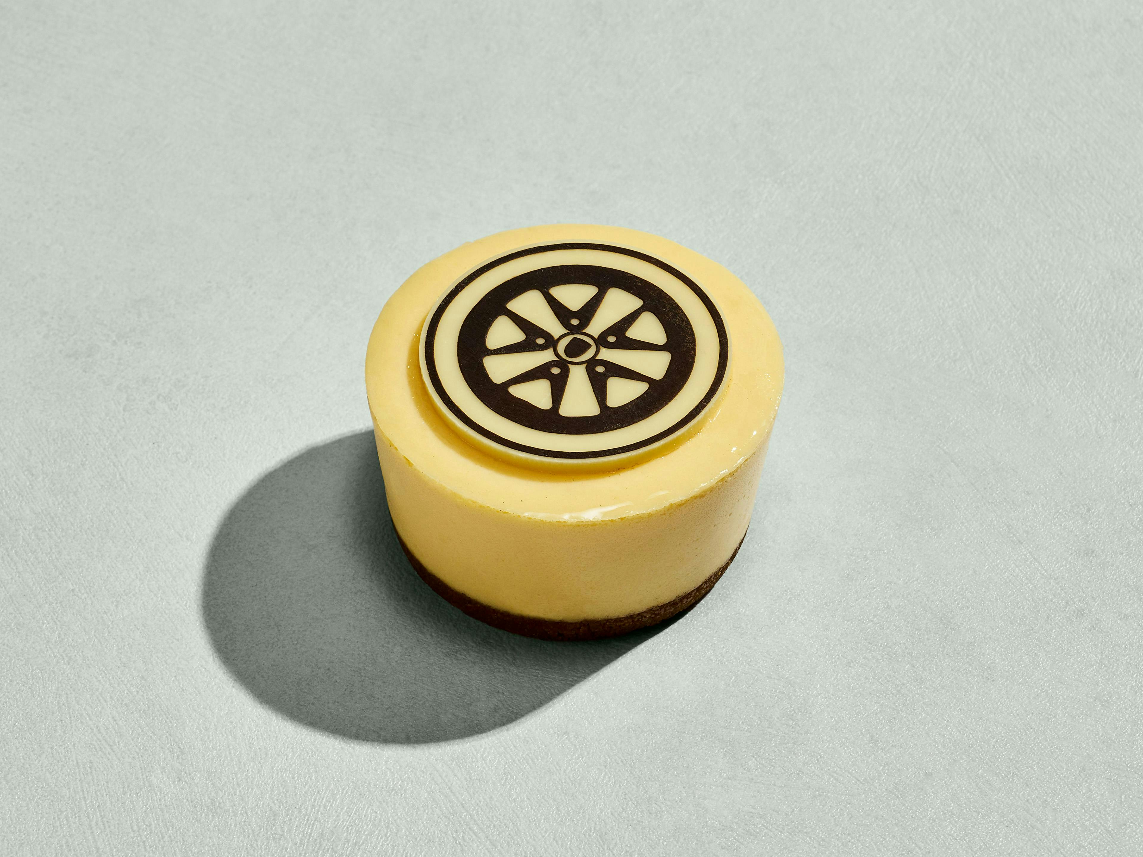 Circular New York cheesecake with a biscuit base, decorated with a round chocolate disc printed with the Porsche Fuchs wheel (Fuchsfelge).