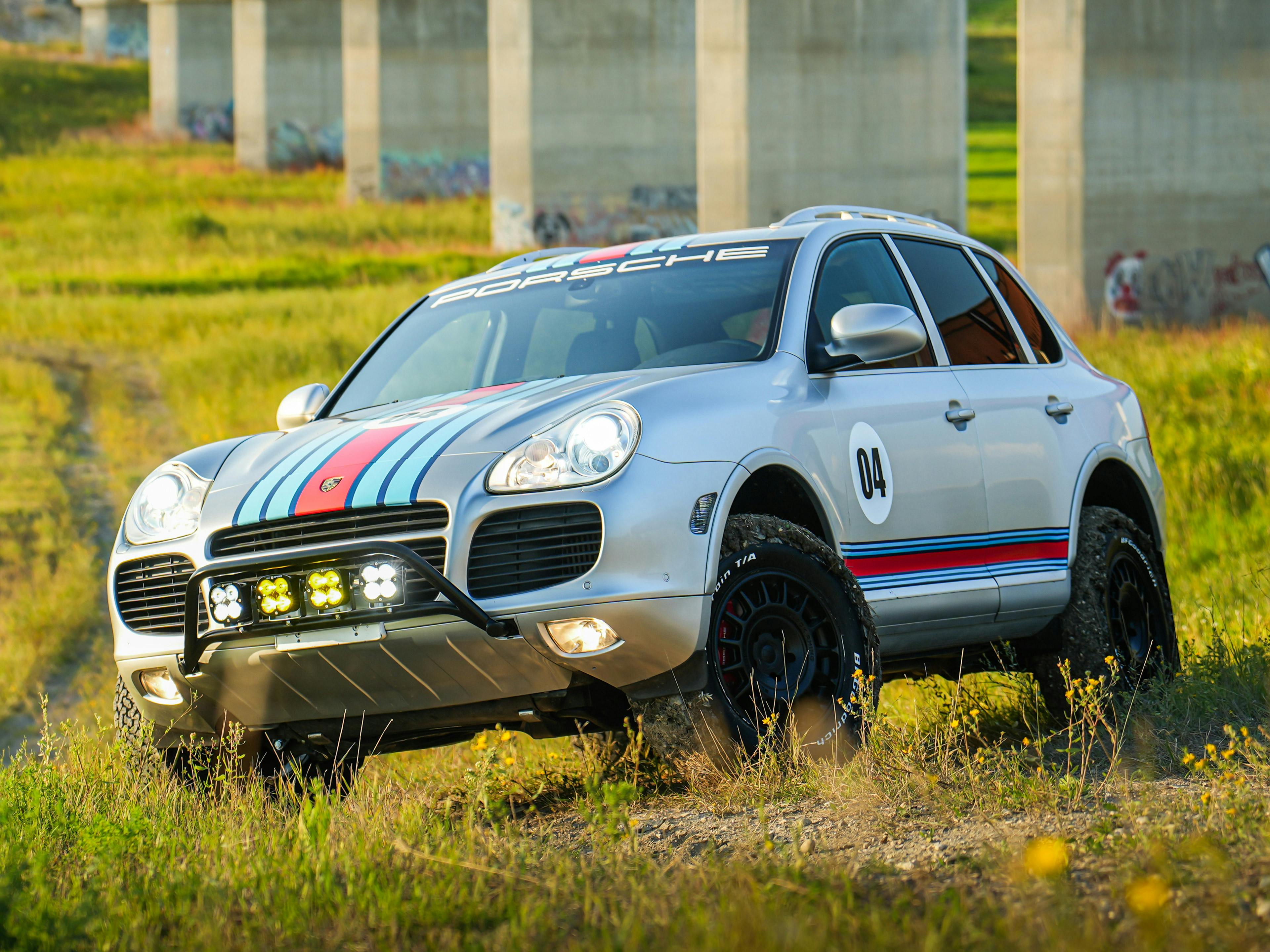 A rear shot of a silver first-generation Porsche Cayenne in a clean, brightly-lit service bay.