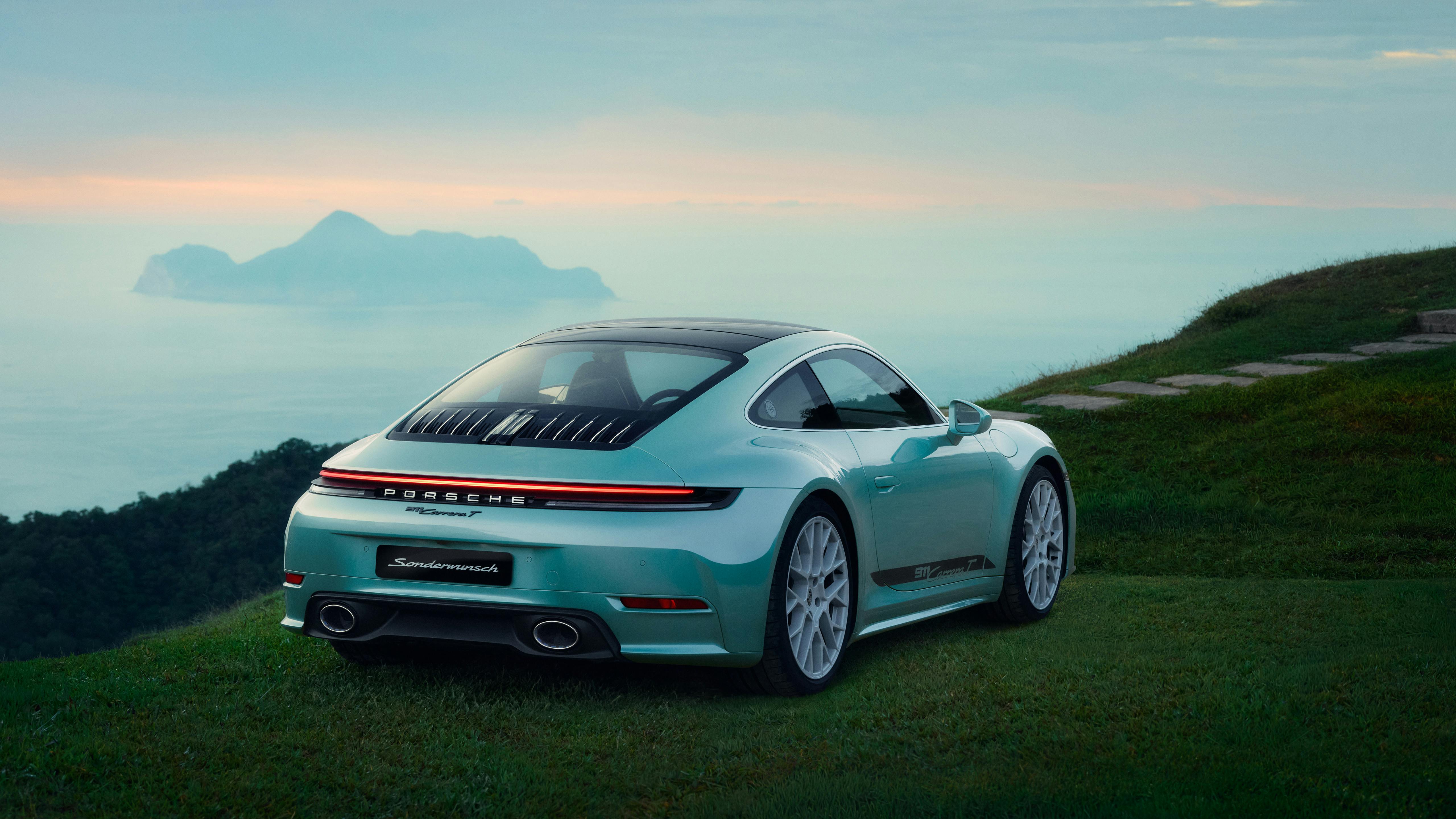 A turquoise Porsche 911 Carrera T parked on a grassy hill, rear view with taillight strip, sea and island in distance.