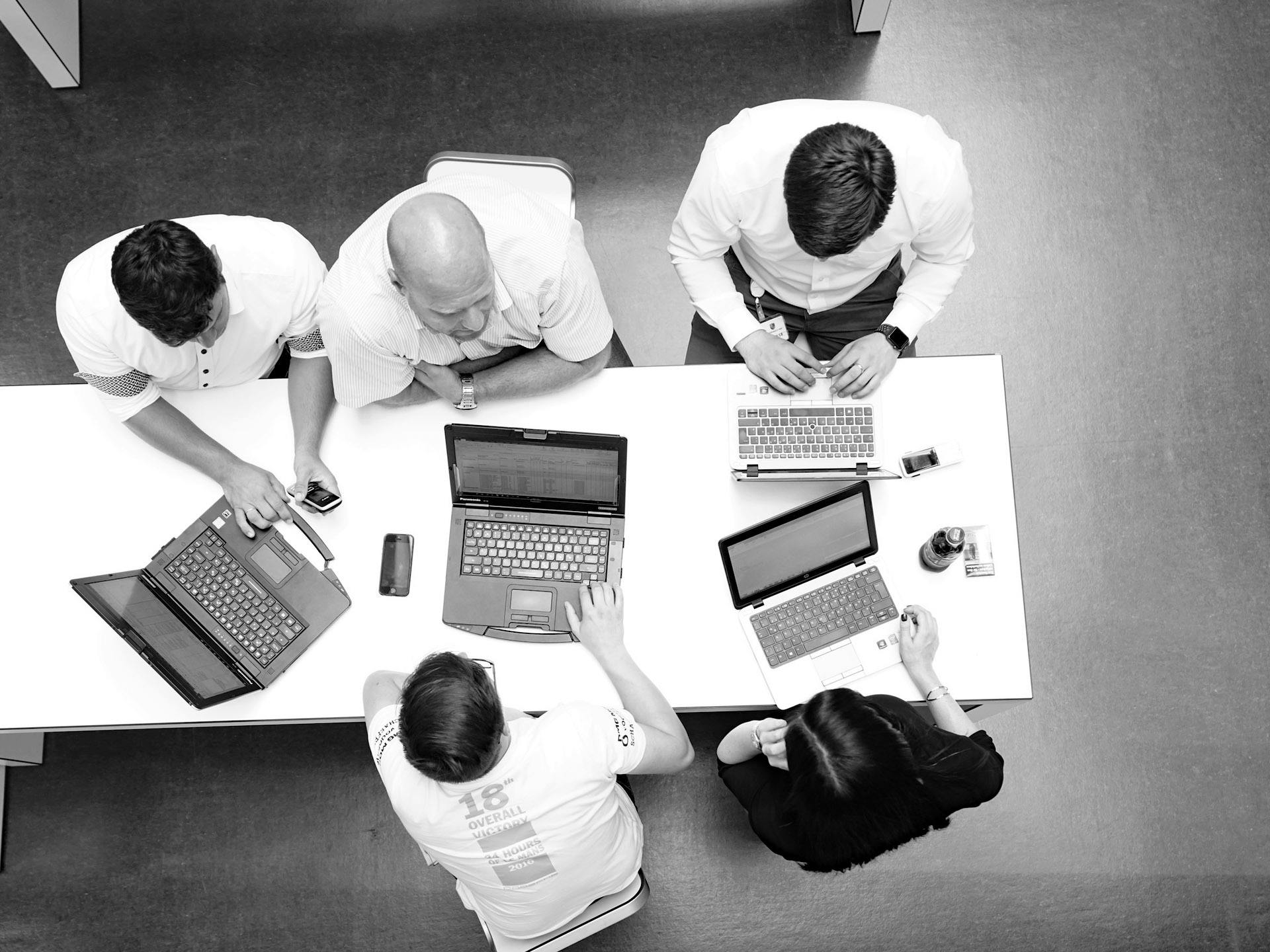 Black-and-white photo: overhead view of several Porsche employees at a table with laptops.