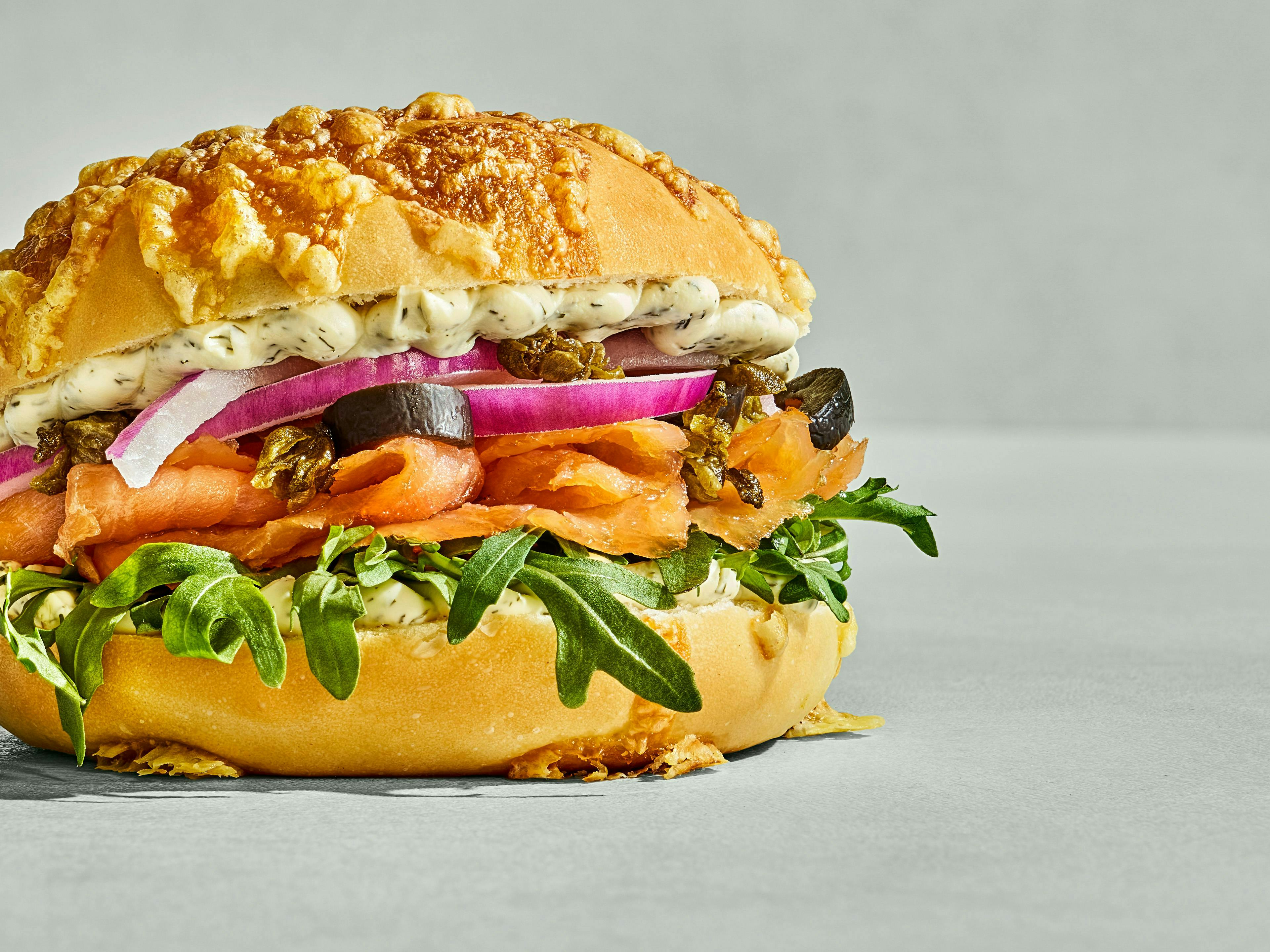 Sandwich with smoked salmon, rocket, red onion, olives and herb cream on a cheese-crusted bun