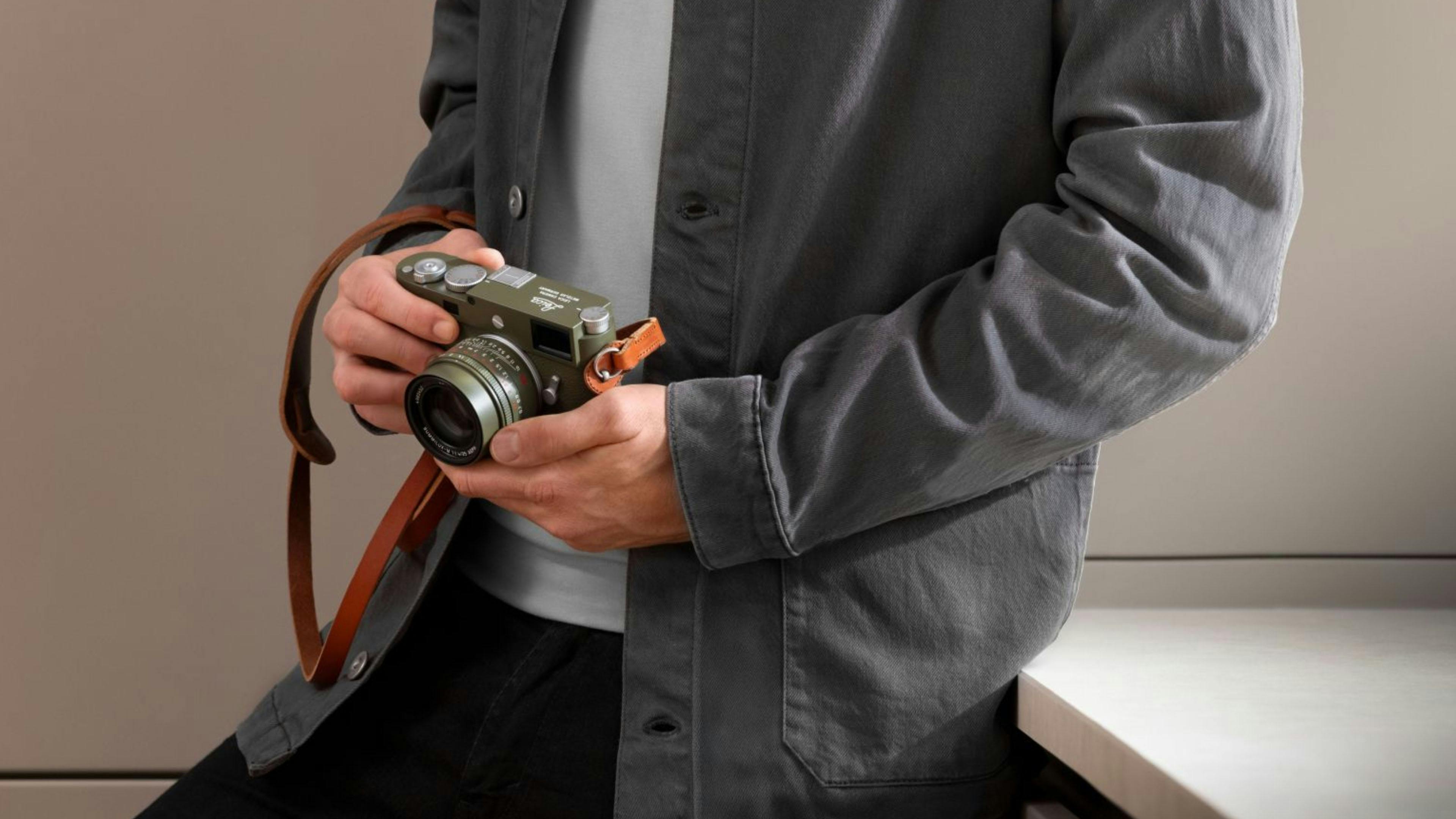 A man posing with a Leica camera, featuring a cognac brown leather strap