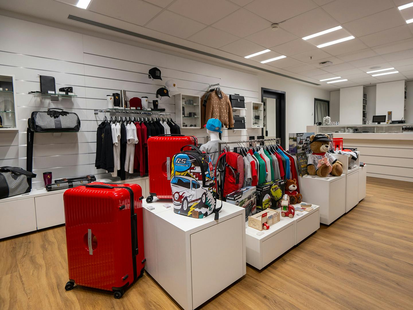 A variety of colourful sales products, from suitcases to teddy bears, are laid out on white, modern dressers.