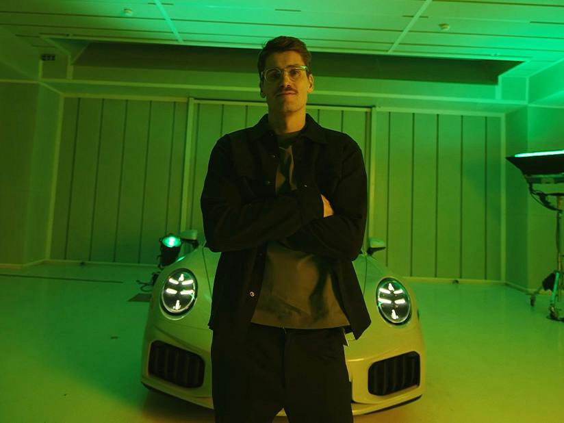 Porsche Mitarbeiter Philipp posiert vor einem Porsche 911 in grünem Licht.