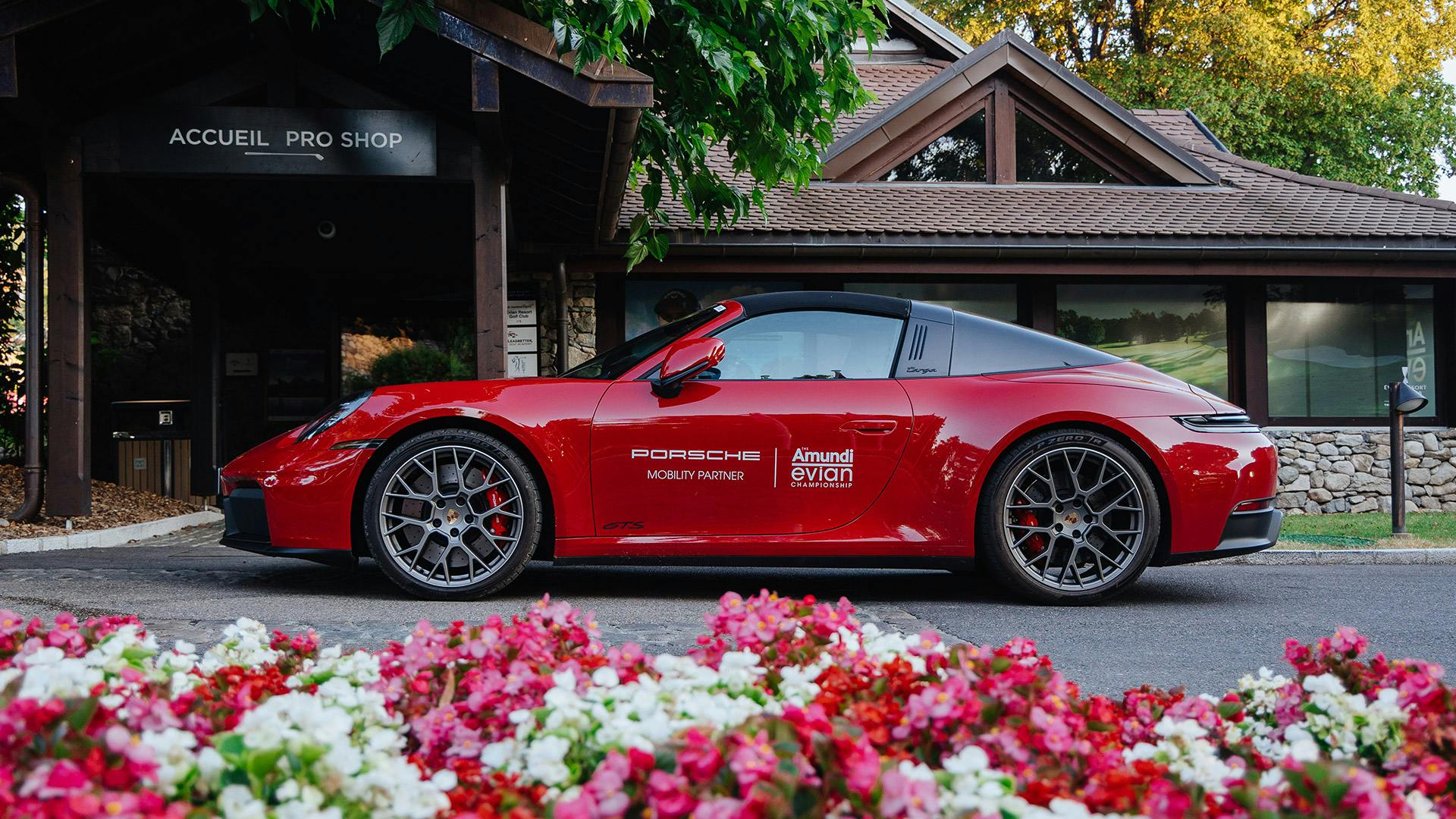 Roter Porsche 911 Targa GTS vor dem Golf-Clubhaus in Evian mit Blumenbeet im Vordergrund.