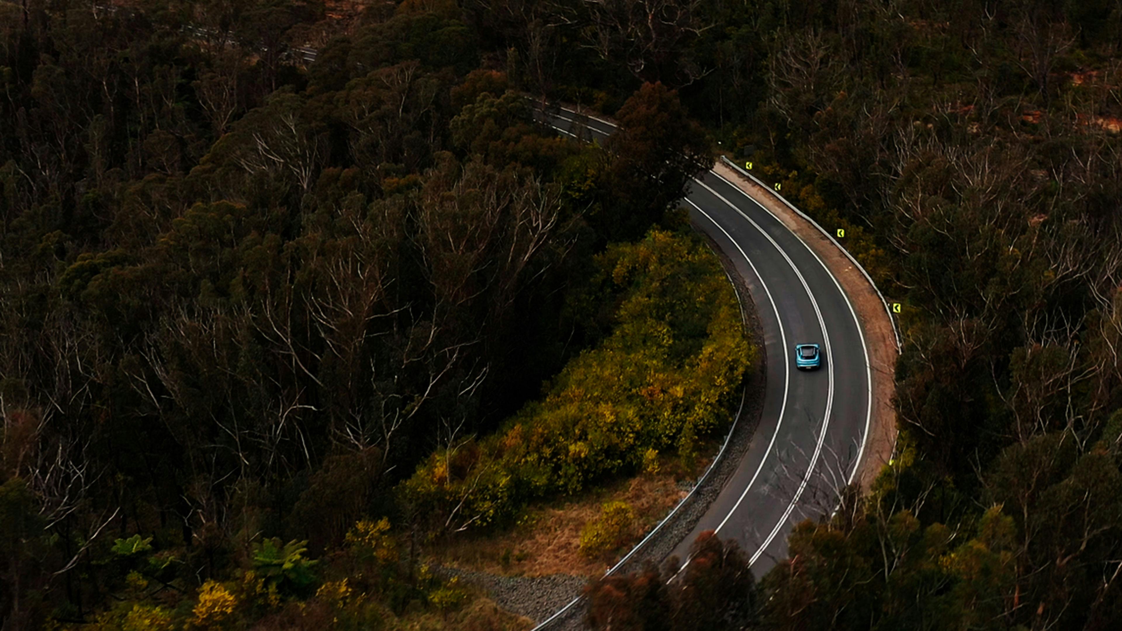 Aerial view of Porsche Taycan driving on winding road surrounded by trees