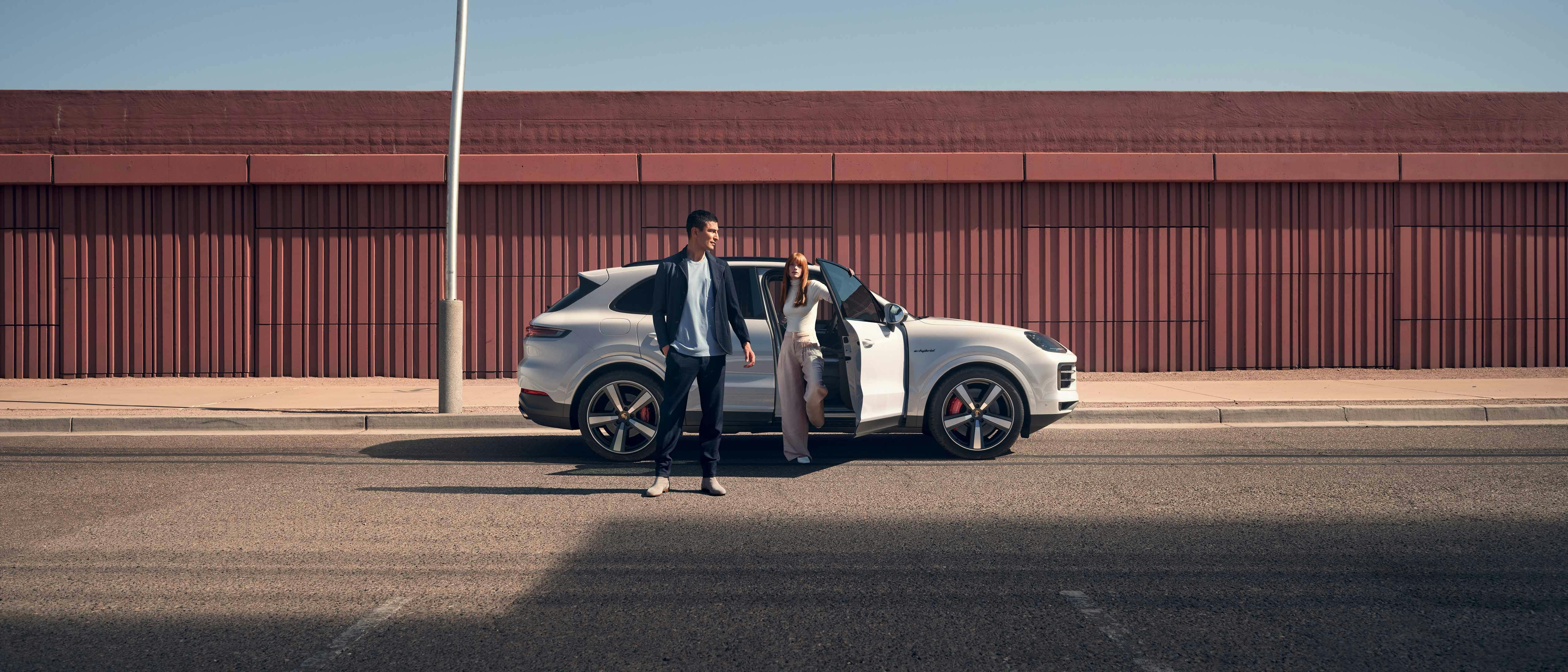 Een man en een vrouw stappen uit een witte Porsche Macan op een parking