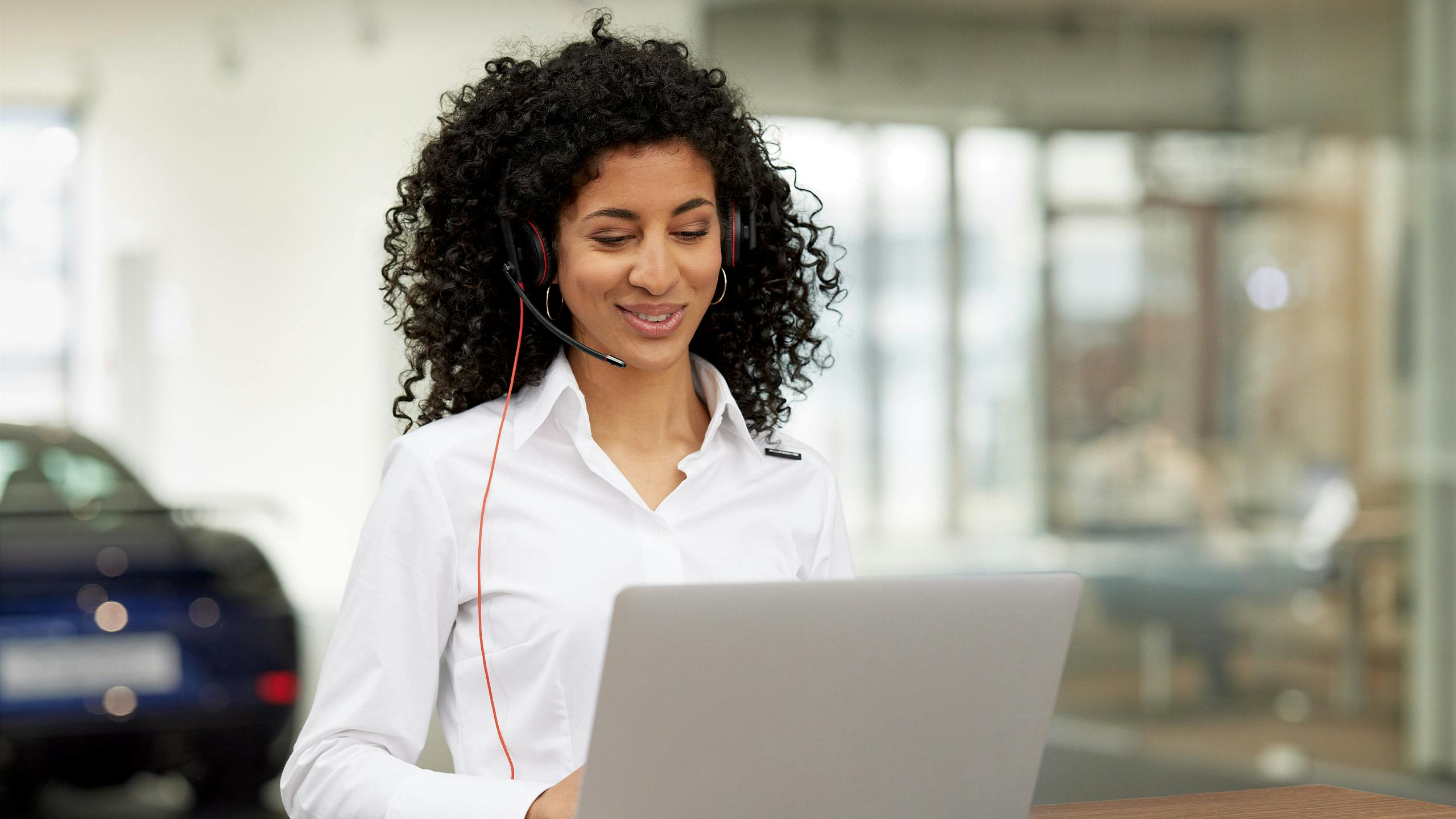 A Porsche service assistant is in a conversation via headphones and looking at her laptop.