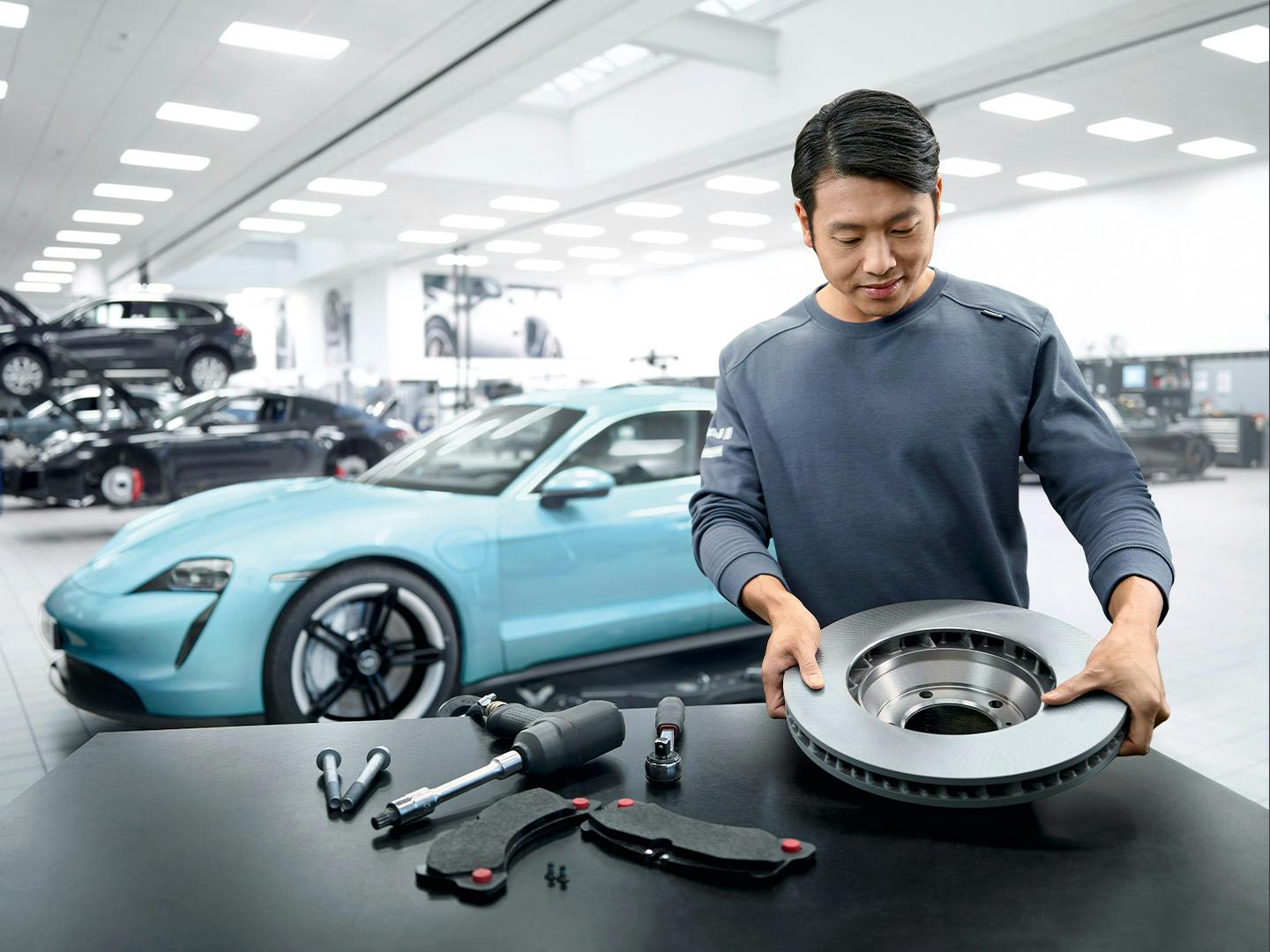 A Porsche workshop employee changes the brake discs. A Taycan can be seen in the background.