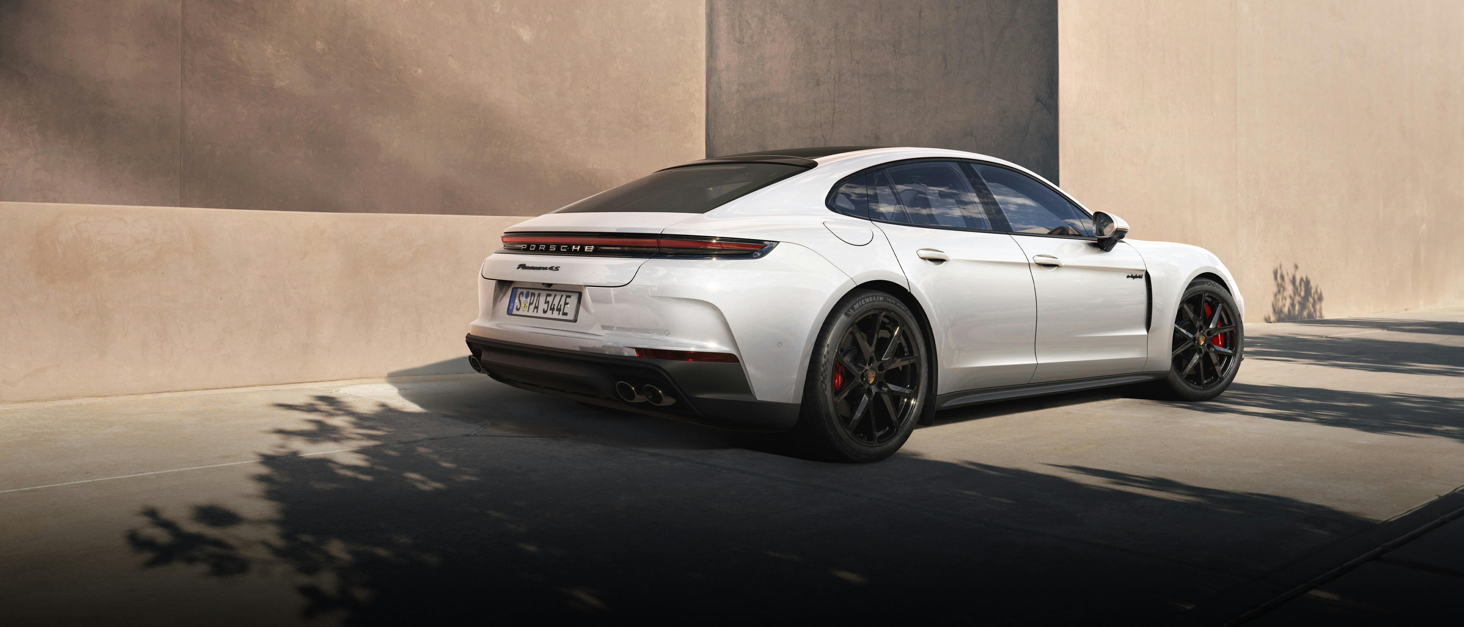The Panamera 4S E-Hybrid parked near a stone coloured, modern building, with the shadows of a nearby tree in the foreground.