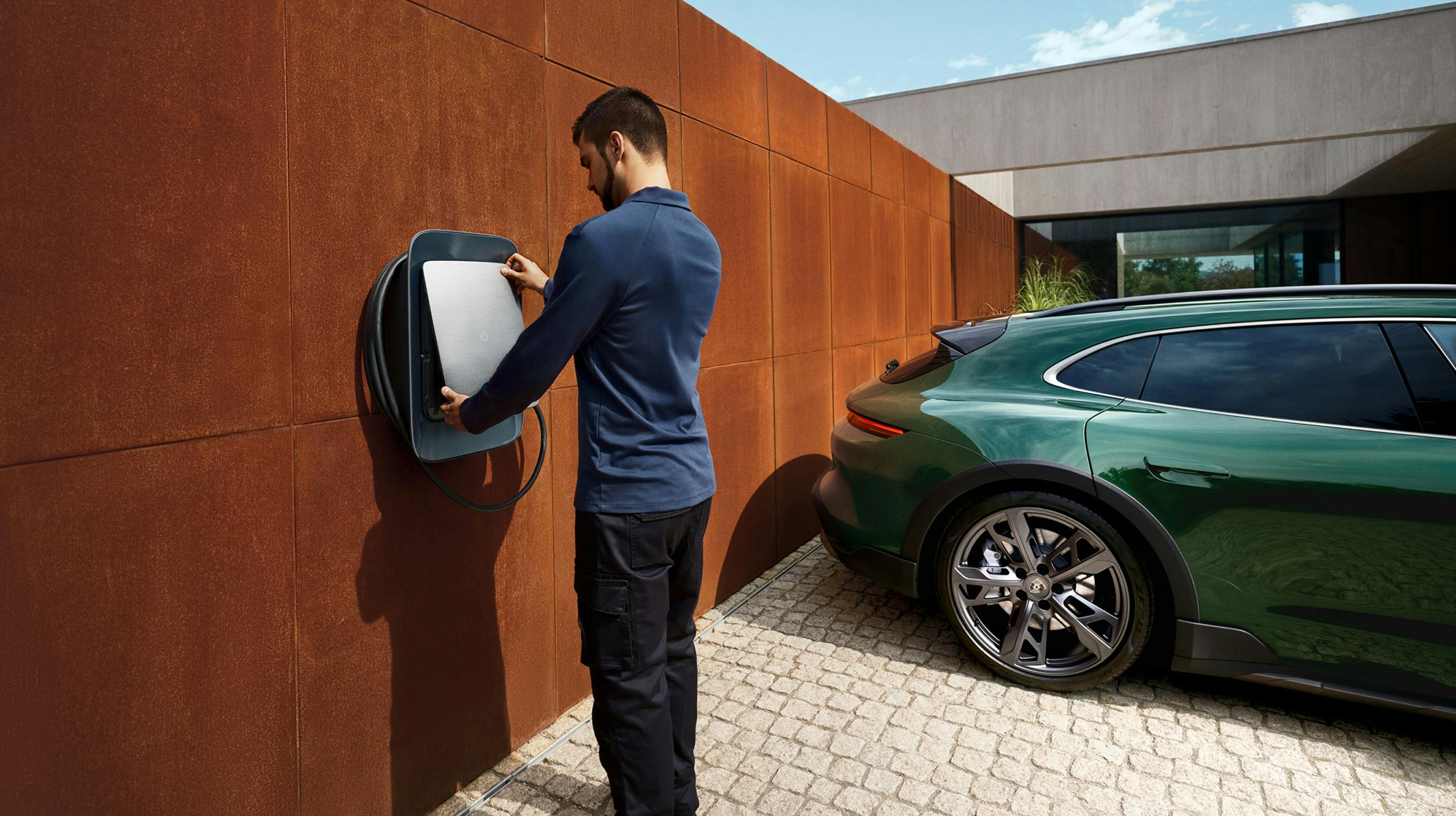 A man opening a Wallbox. A Porsche Taycan Turbo Cross Turismo is in the background.